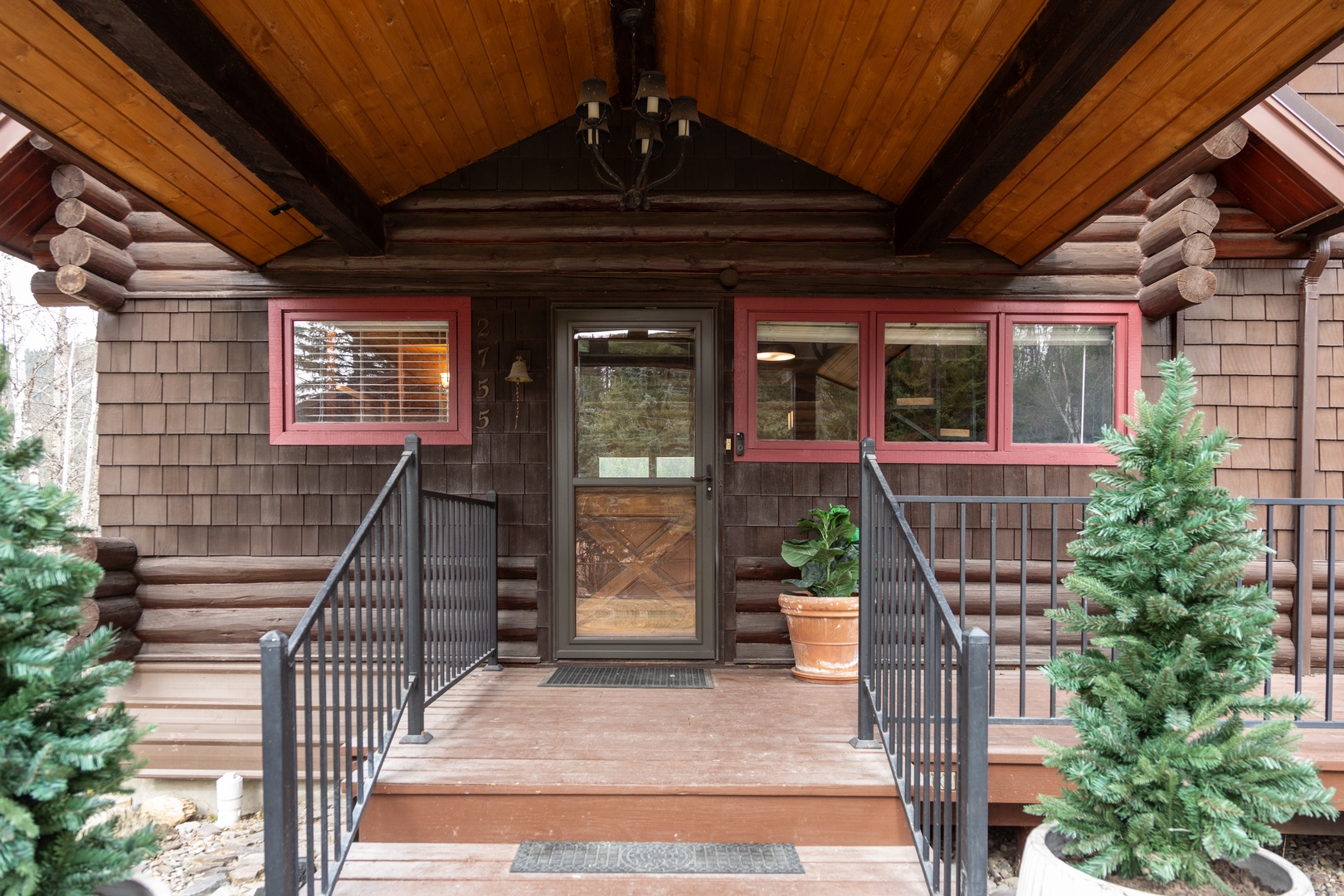 Charming log cabin entrance with rustic wood details and welcoming covered porch surrounded by evergreen landscaping.