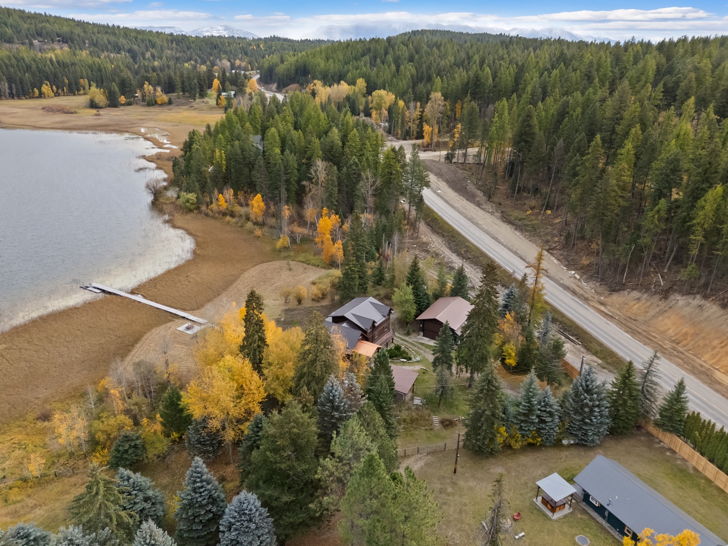 Stunning lakeside retreat nestled among autumn forests, featuring multiple buildings on spacious grounds with water access and scenic mountain backdrop.
