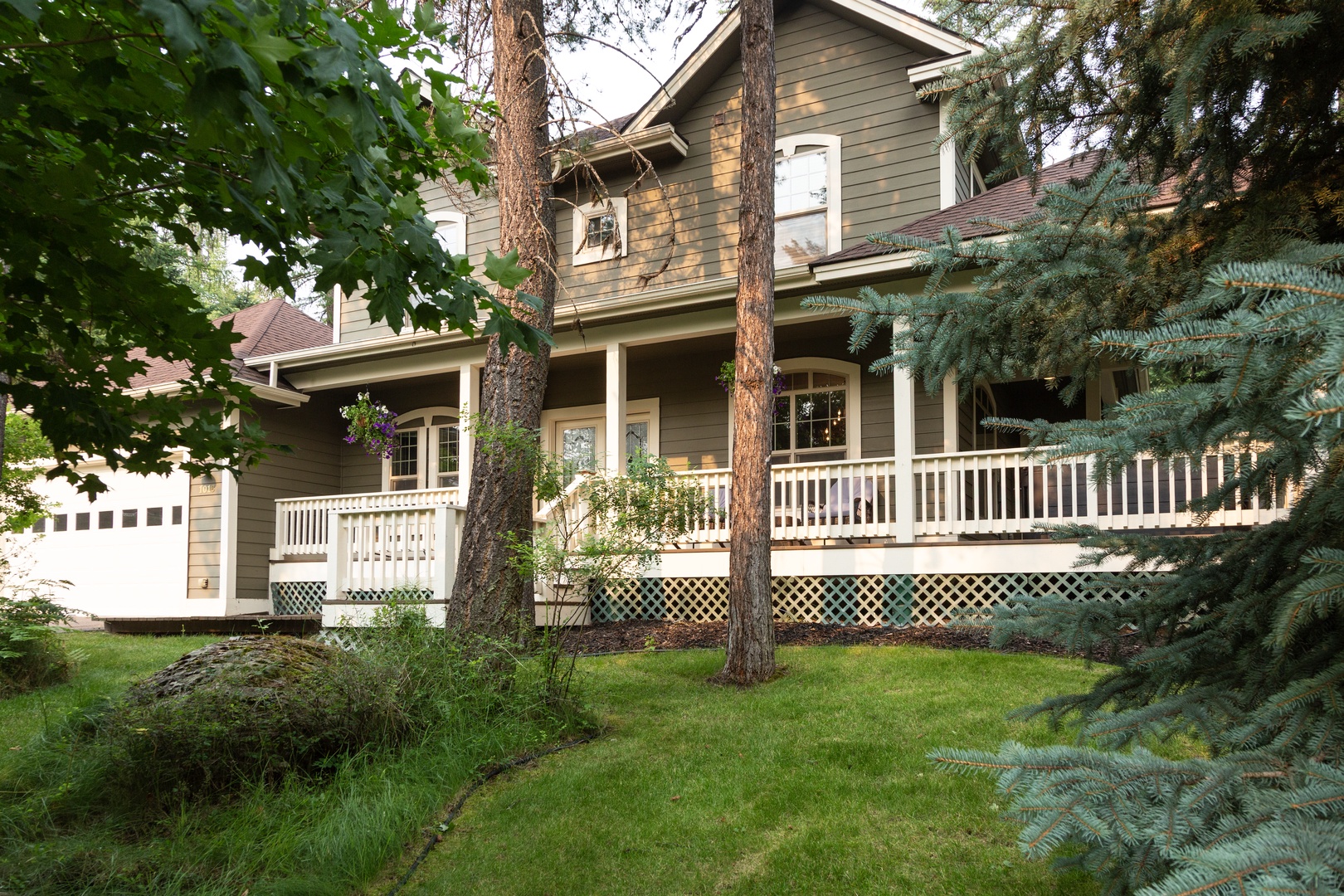 A charming two-story property nestled among mature trees and lush greenery, featuring welcoming wraparound porches and a peaceful natural setting.