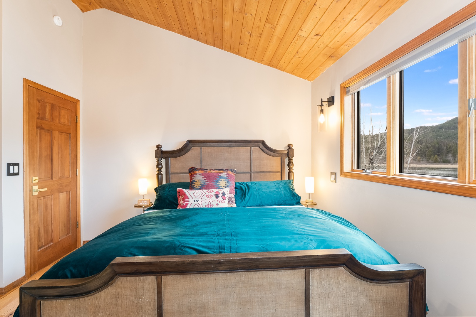 Drift off peacefully in your cozy bedroom with stunning mountain views through large windows and warm wood ceiling details.