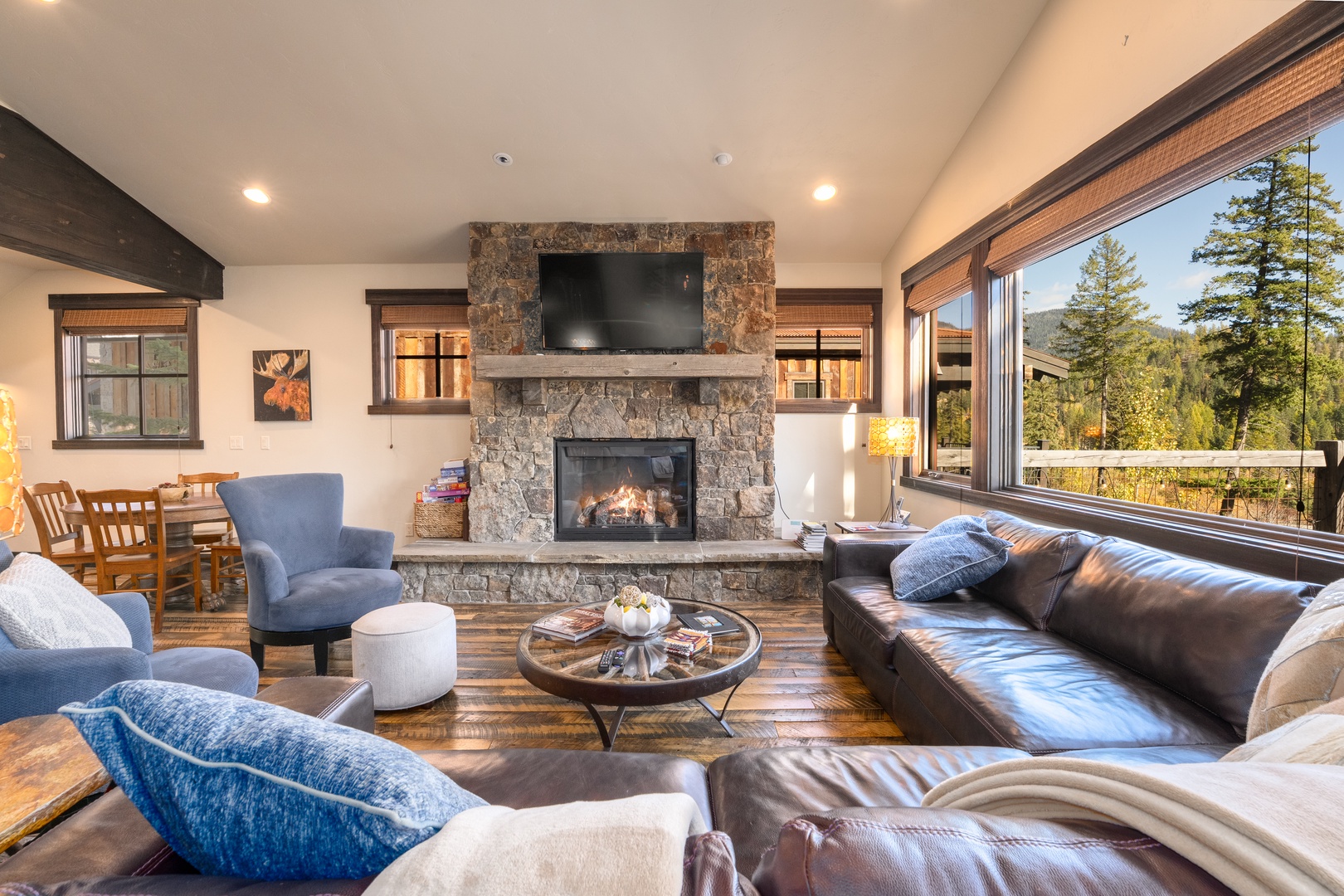 Unwind in this inviting living area where a stone fireplace anchors your mountain retreat. Large windows frame stunning forest views, flooding the space with natural light as you relax on plush seating and plan your next adventure.