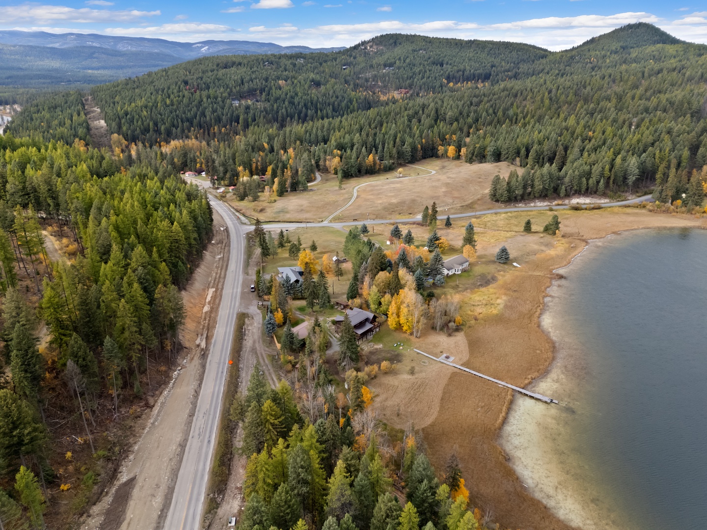Aerial view reveals a pristine lakeside location nestled among forested mountains, with autumn colors painting the landscape in golden hues.