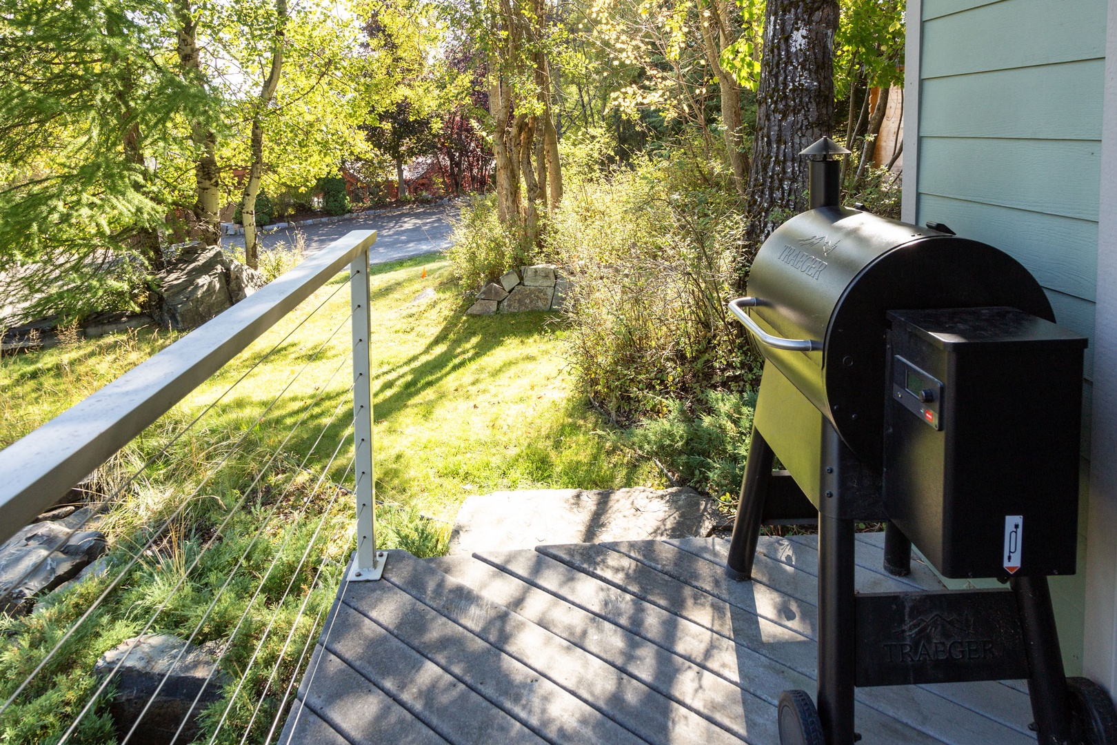 Your private deck is set up for outdoor cooking with a smoker grill, surrounded by trees and natural greenery. Step outside to prepare your favorite meals in fresh air and sunlight.