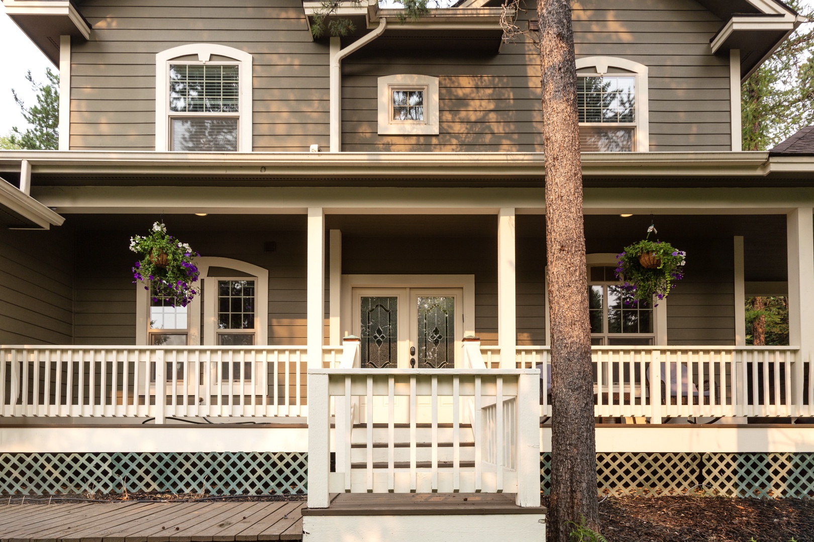 Charming two-story exterior with welcoming covered porch, elegant white railings, and decorative front entrance surrounded by mature trees.