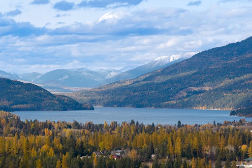 Stunning mountain landscape with pristine lake nestled among forested hills and snow-capped peaks in the distance.
