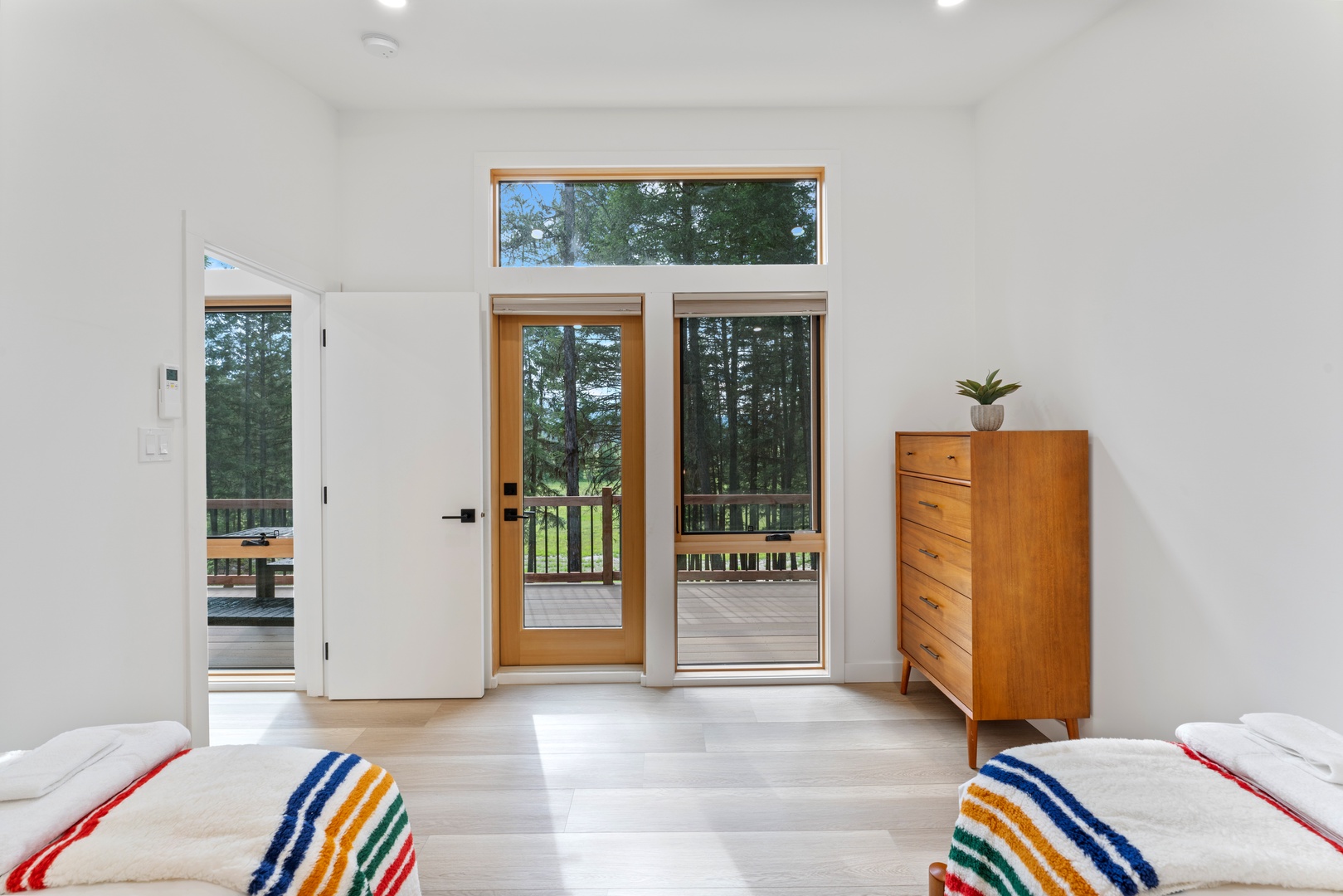 Step into your bright, modern retreat where floor-to-ceiling windows frame forest views and your private deck awaits just beyond the glass doors.