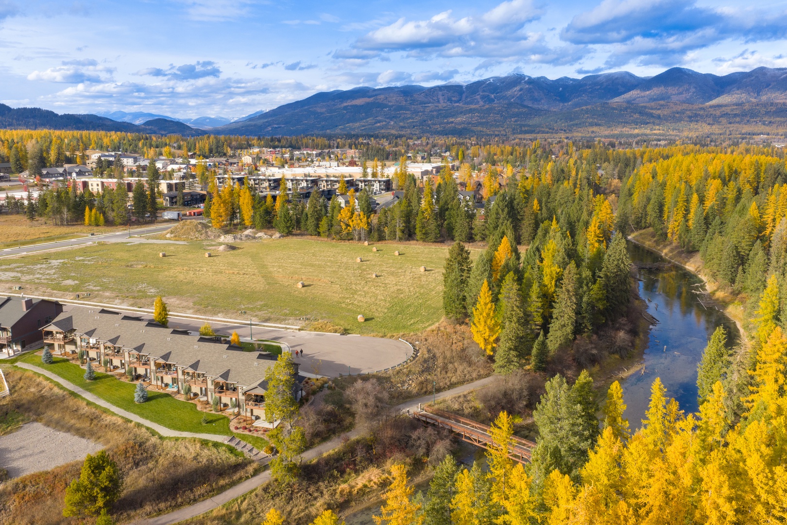 Aerial view of mountain resort community nestled among golden autumn foliage with river and dramatic peaks backdrop.