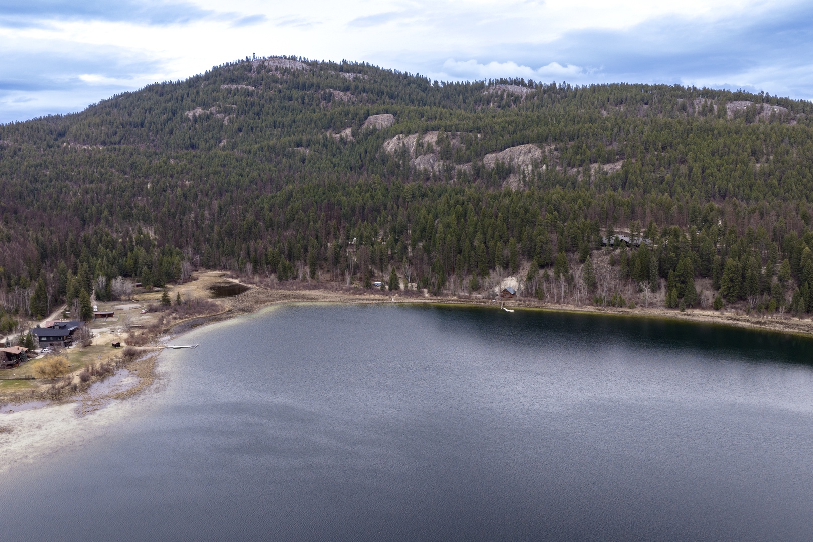Aerial view showcases the pristine mountain lake surrounded by dense forest and rolling hills in this scenic location.