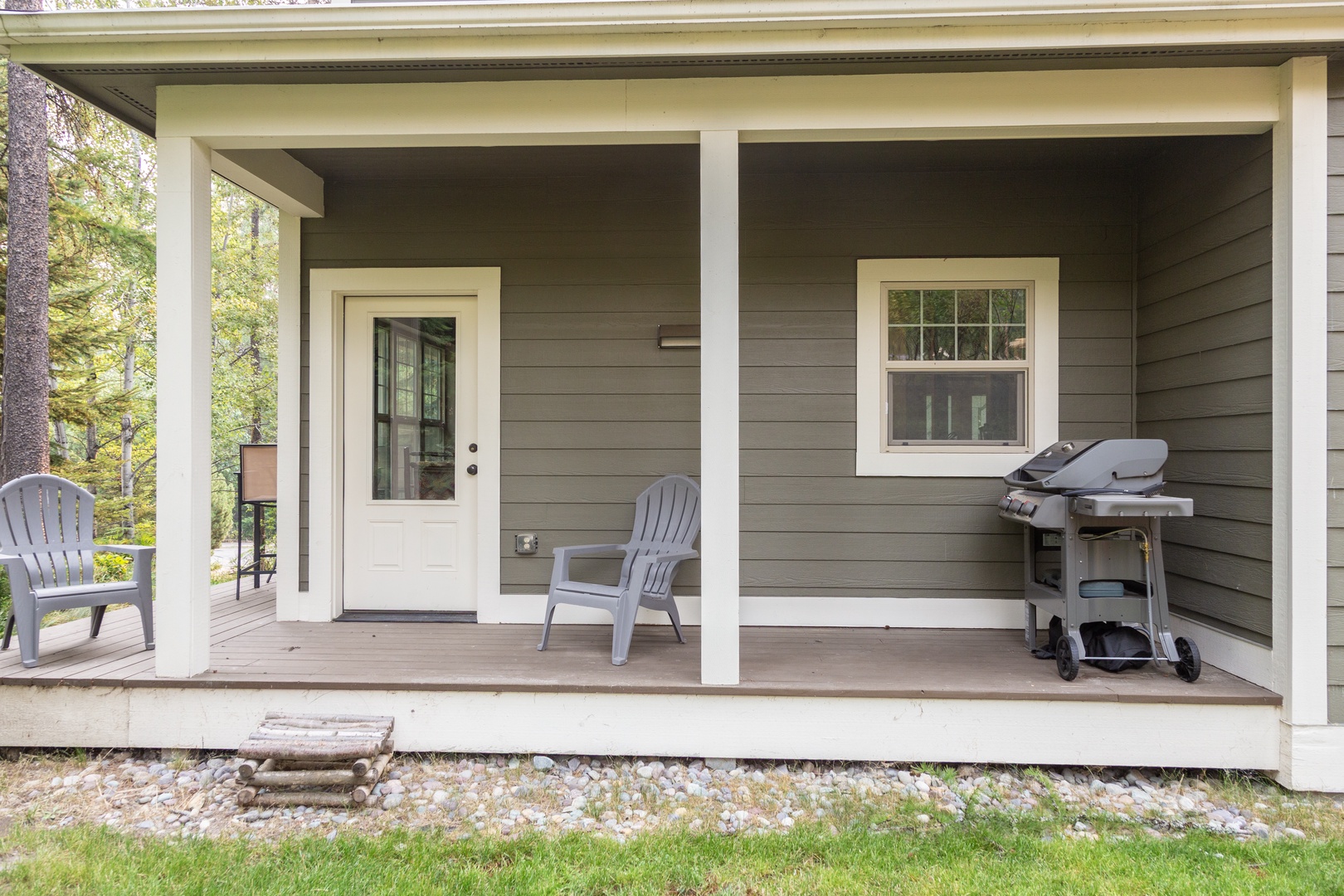 The covered front porch offers a welcoming entryway, complete with outdoor seating and a convenient gas grill—perfect for cooking up meals while surrounded by peaceful woodland scenery.