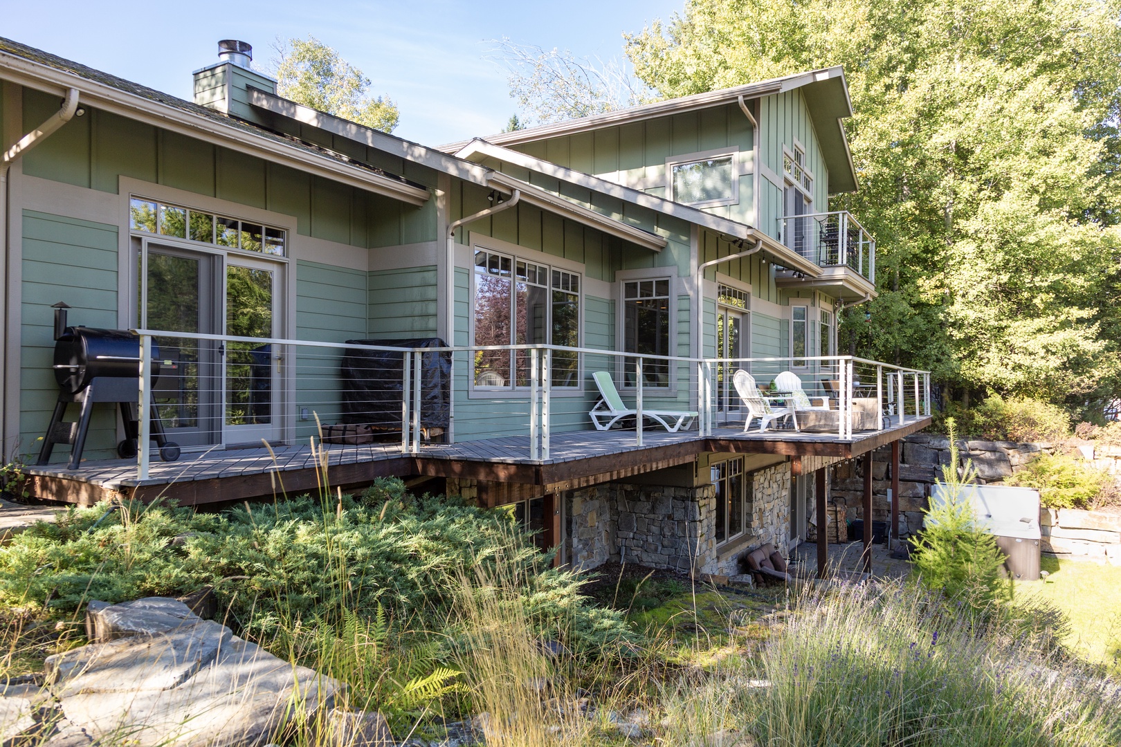 A charming hillside retreat surrounded by mature trees and native landscaping. The property features a spacious deck with modern cable railing, offering an ideal spot for outdoor dining and relaxation in a serene natural setting.