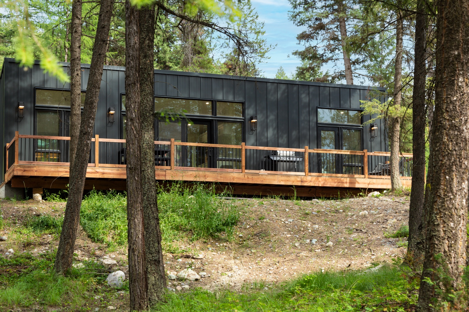 Modern forest retreat with sleek dark siding and expansive deck nestled among towering trees.