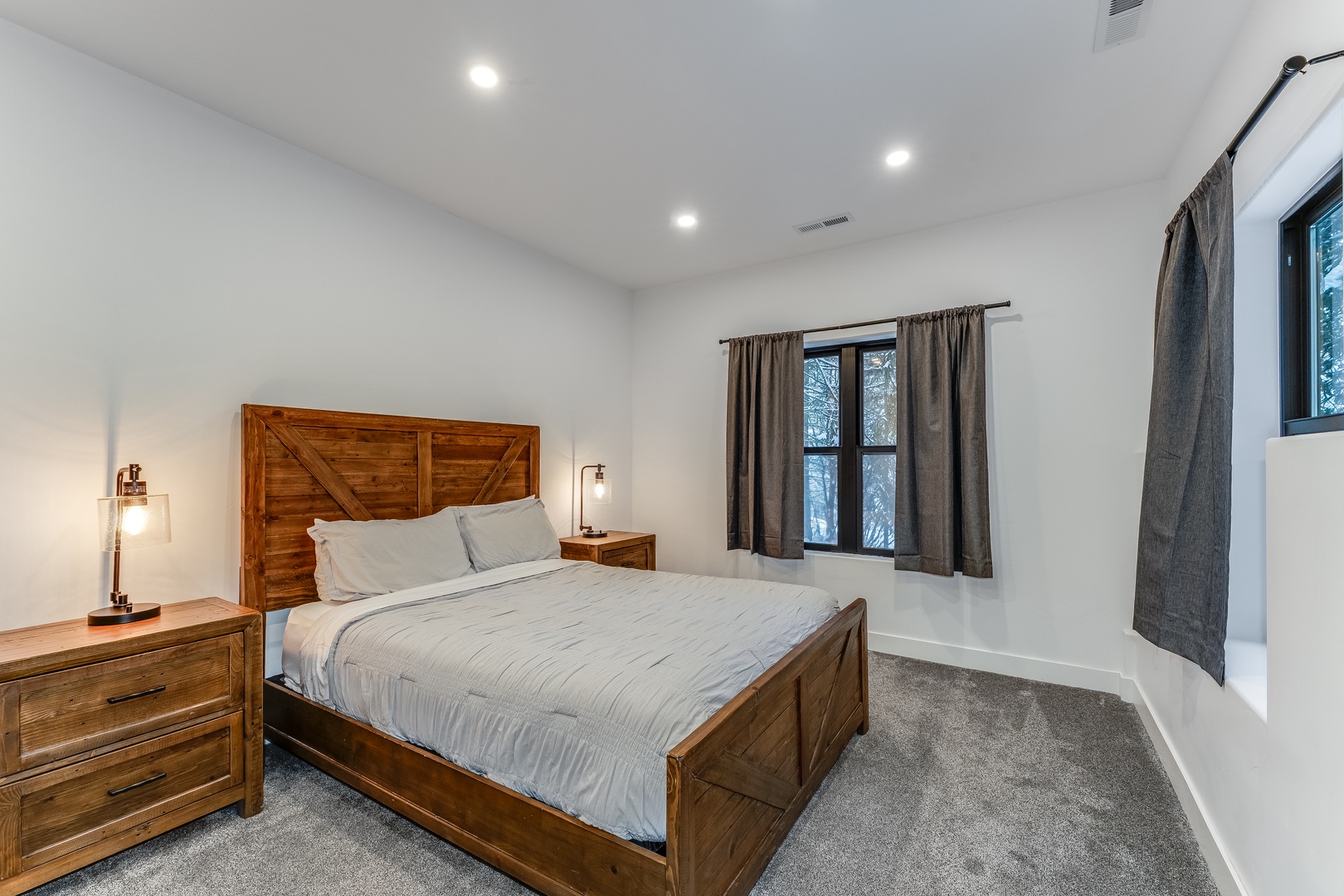 Drift off in this inviting bedroom featuring rich wood furniture, soft lighting, and peaceful views through large windows.