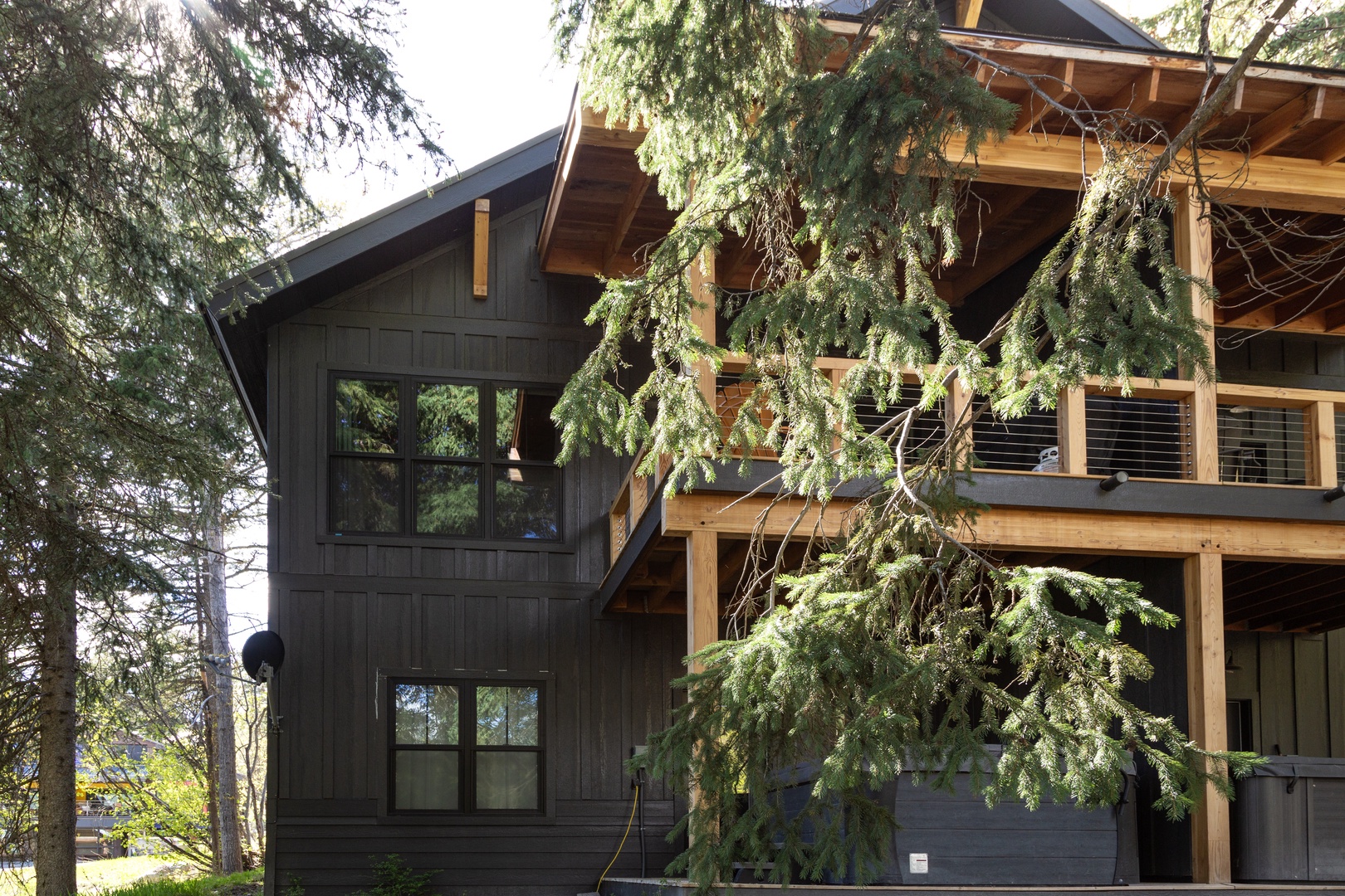 A modern timber-framed retreat nestled among towering evergreens. Dark board-and-batten siding contrasts with warm natural wood beams and railings. Multi-level balconies overlook a peaceful, forested setting.