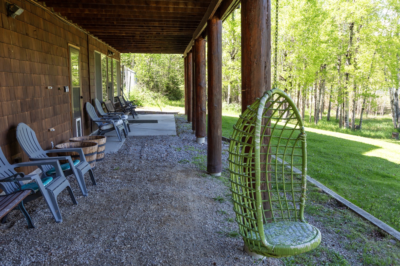 Unwind in your private covered porch with Adirondack chairs and a charming hanging swing, overlooking serene woodlands and lush green lawns perfect for peaceful mornings.