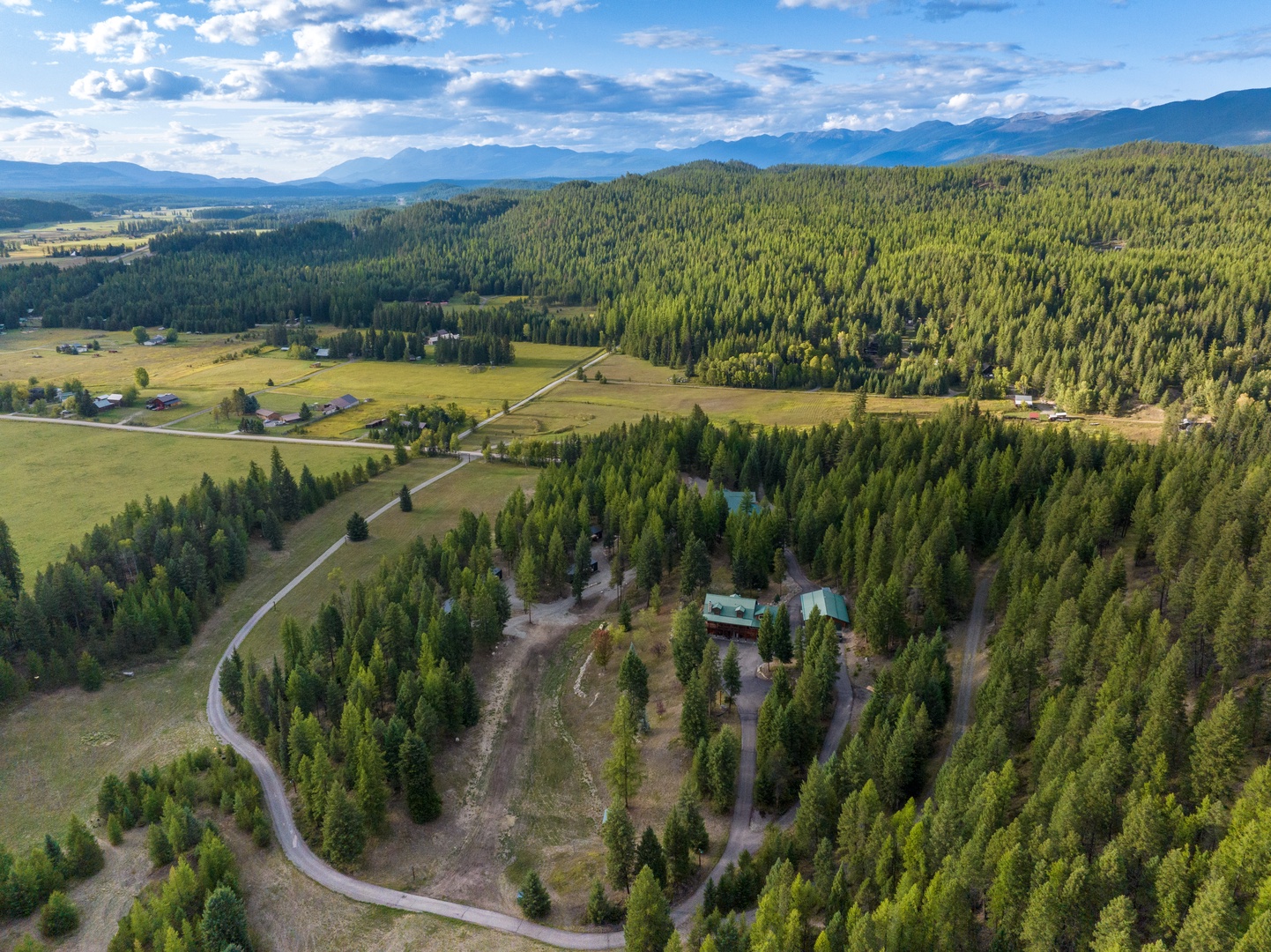 Aerial view showcasing the property nestled among dense forests with mountain ranges and rural valleys stretching into the distance.
