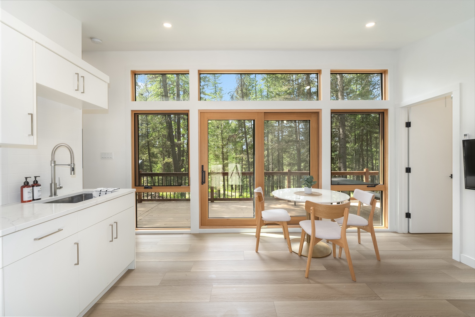 Gather around this inviting dining space where sunlight pours through floor-to-ceiling windows, framing peaceful woodland views. Step onto your private deck surrounded by nature's tranquility.