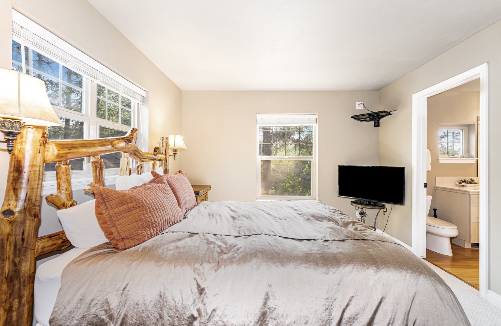 Unwind in your cozy bedroom with rustic log-style charm, where natural light streams through large windows and your private en-suite awaits for added comfort and convenience.
