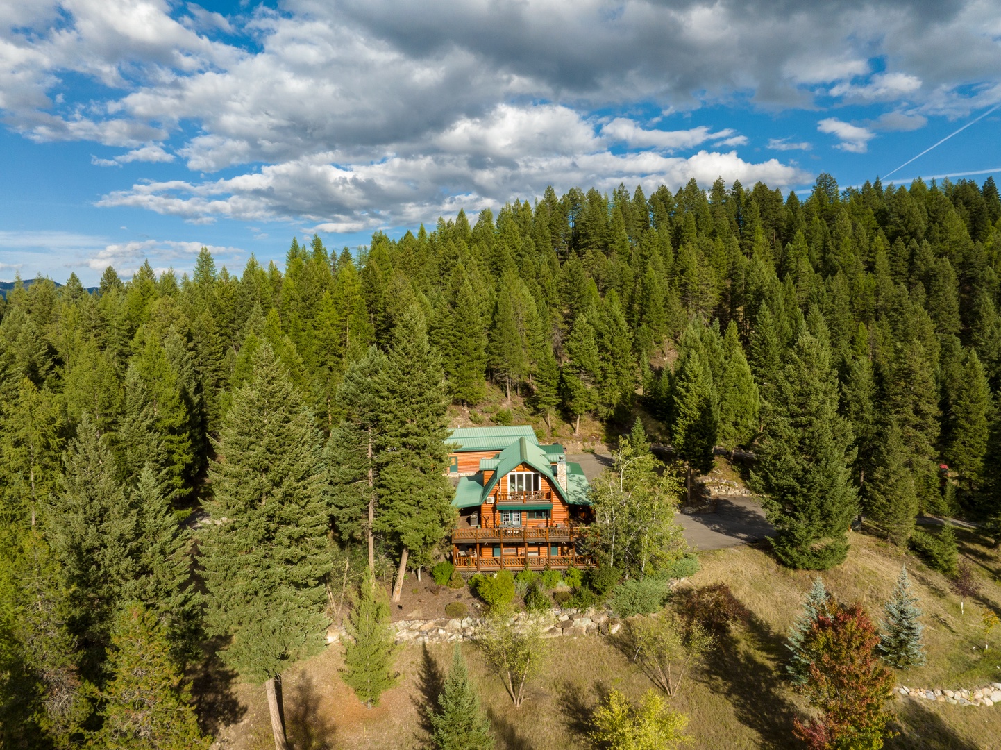 A picturesque log cabin with a distinctive green roof nestled within dense forest terrain, offering seclusion and mountain charm in a tranquil wooded setting.