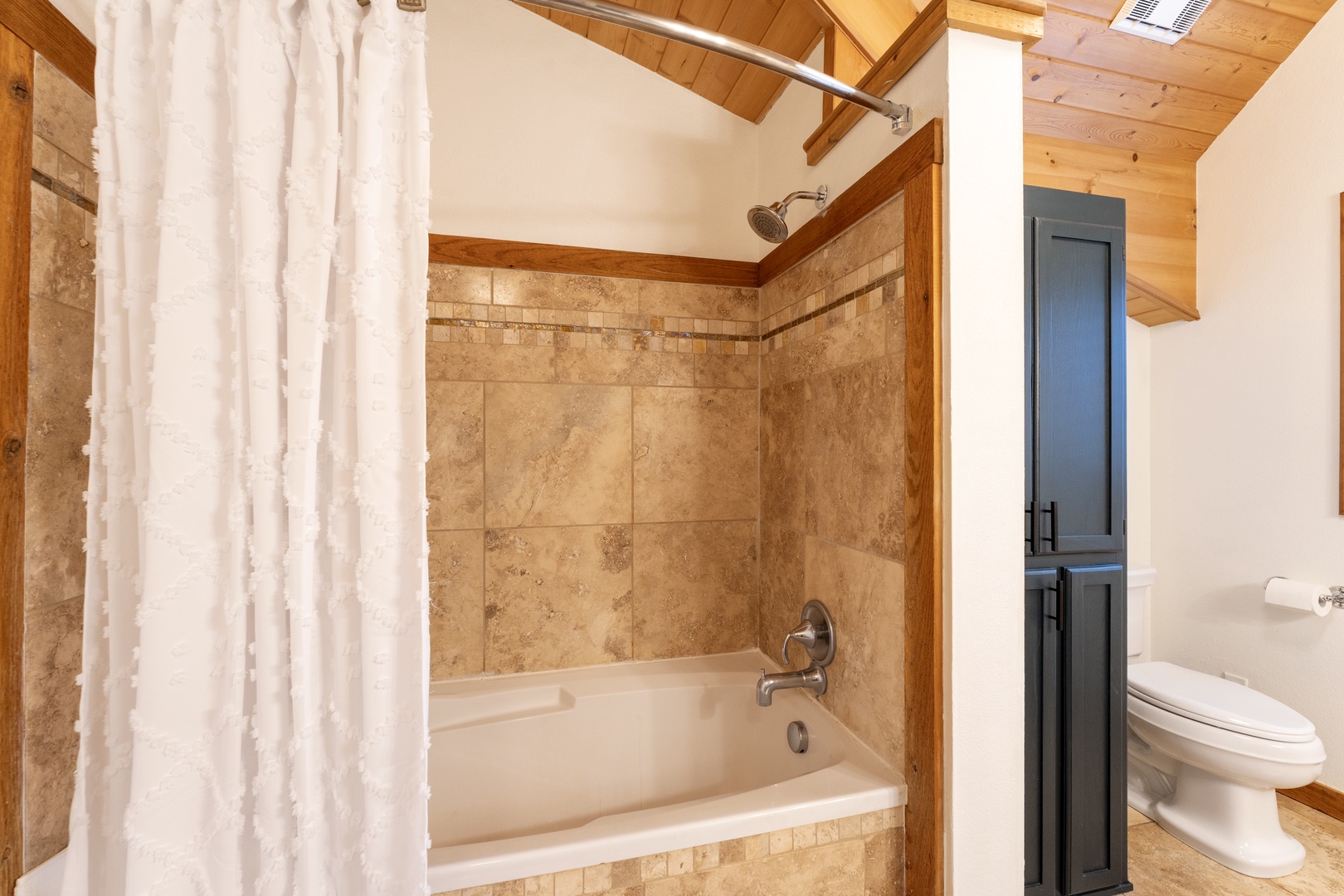 Unwind in your elegant bathroom featuring a deep soaking tub, beautiful stone tile work, and rustic wood beam details.