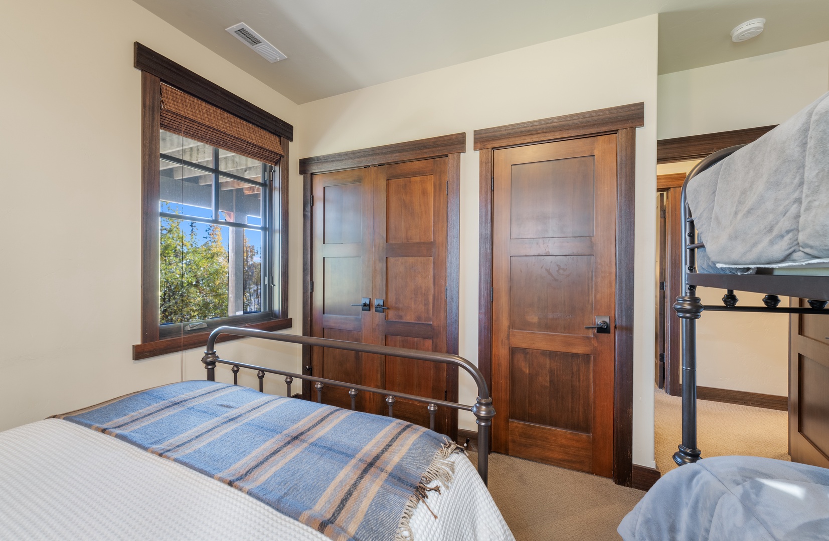 Rest well in this cozy bedroom with a comfortable metal-frame bed, warm wood cabinetry, and a window that lets in natural light and views of the surrounding greenery.
