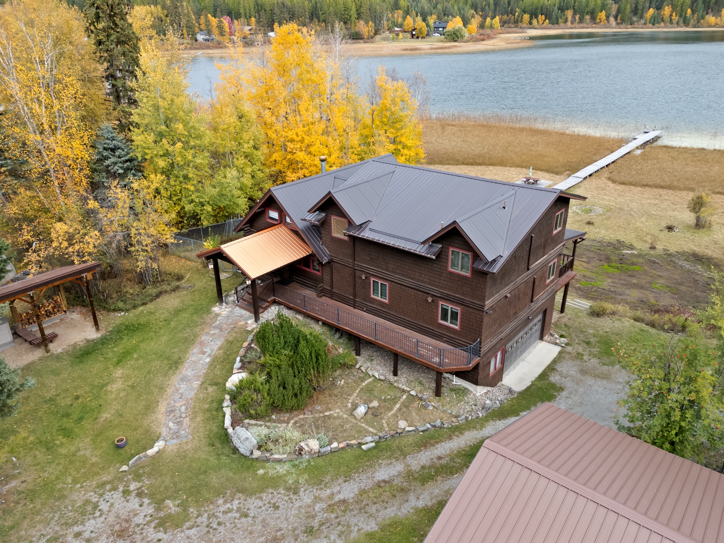 Stunning lakefront property nestled among vibrant autumn foliage, with a private dock extending into serene waters surrounded by golden aspens.