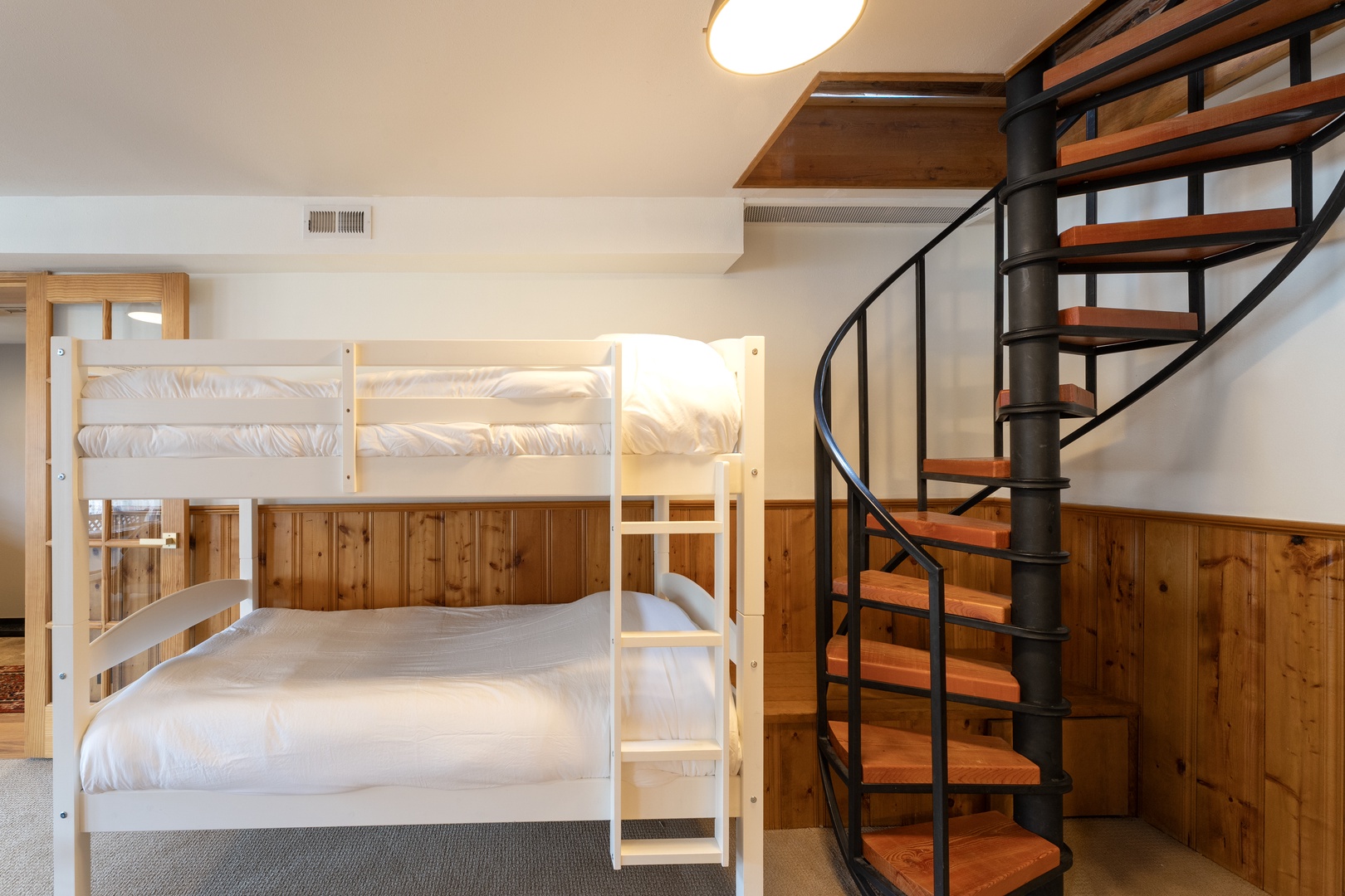 Settle into your cozy bunk bed beneath warm wood accents, where the spiral staircase leads to more adventures above.