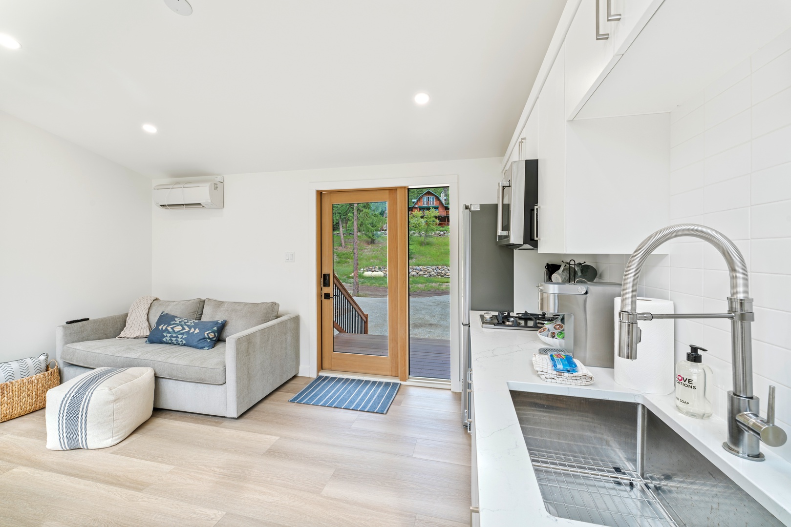 Your bright, modern retreat features a fully equipped kitchen and cozy living area with peaceful garden views through glass doors.