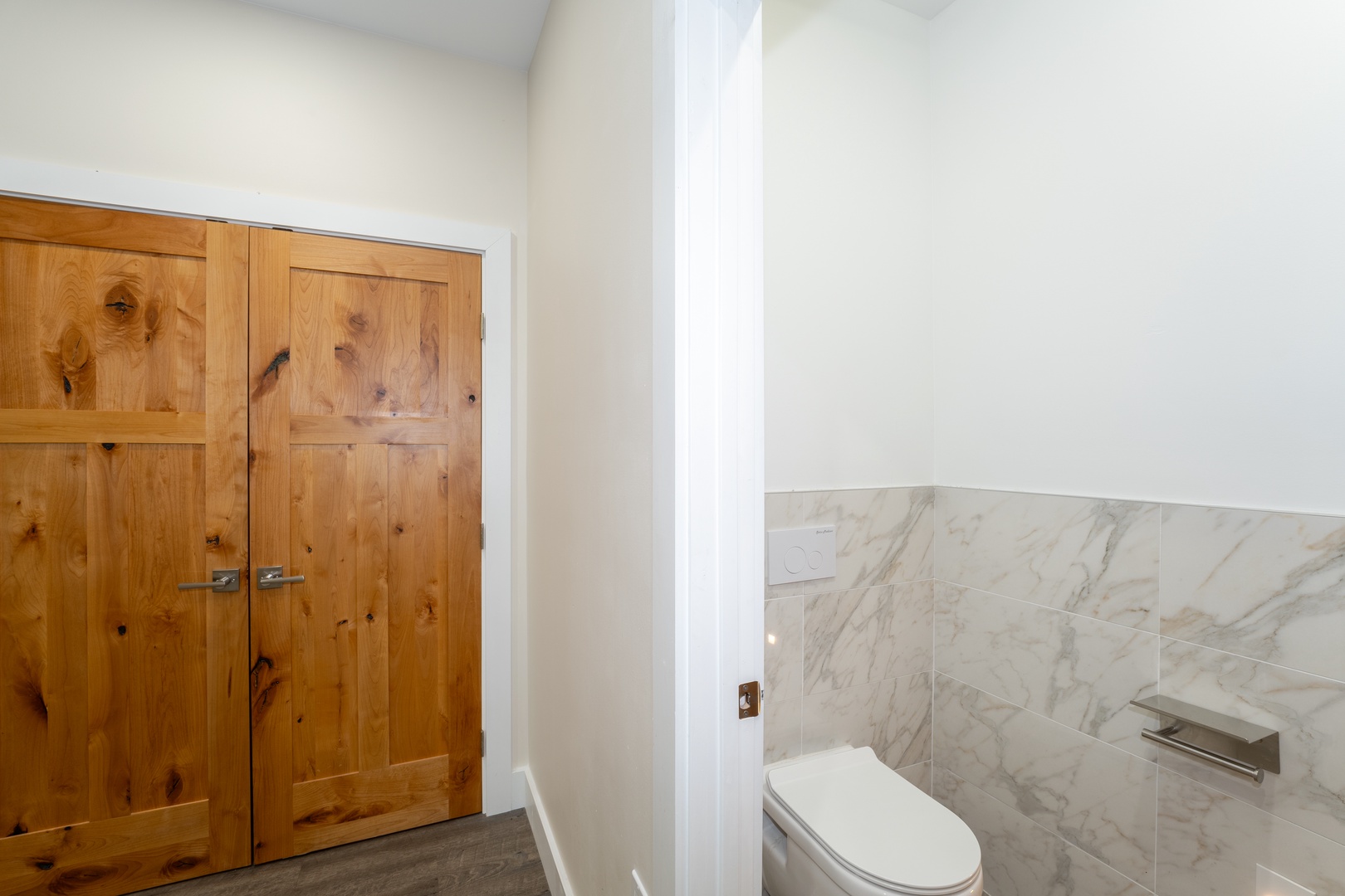 Modern powder room with elegant marble tiling, nestled beside rustic wooden doors that add warmth to your private suite.