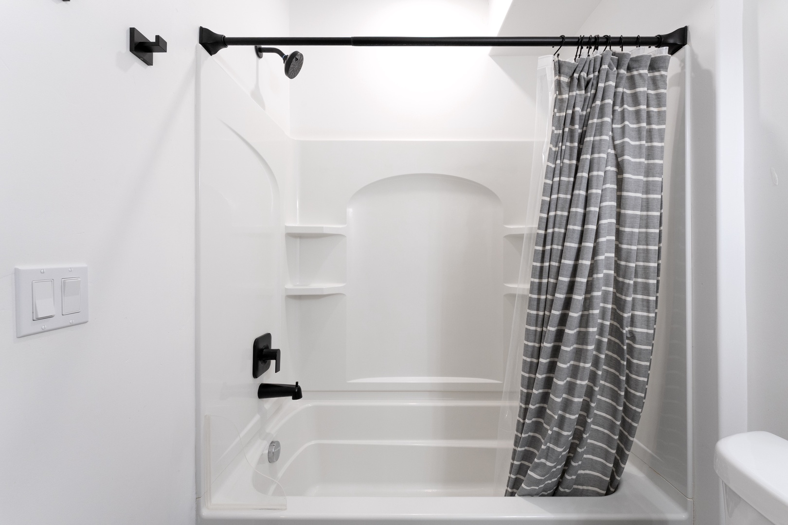 Step into your pristine bathroom with a spacious tub-shower combo, complete with stylish striped curtains and modern fixtures.
