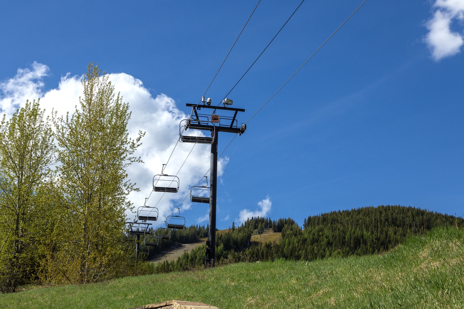 Ski lift ascending toward forested mountain slopes under blue skies—a quiet scene marking the area's winter recreation access and off-season tranquility.