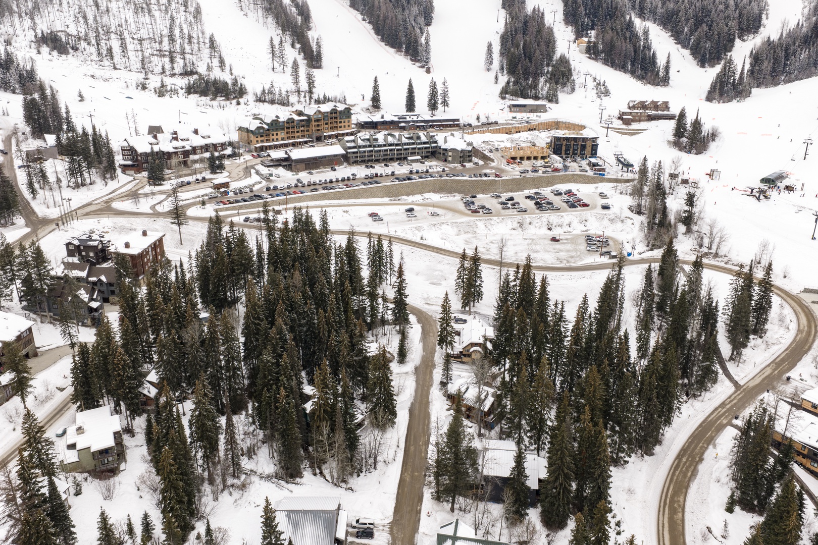 Aerial view of a mountain ski resort nestled in snow-covered valleys with ski slopes, lodge facilities, and parking areas visible below.