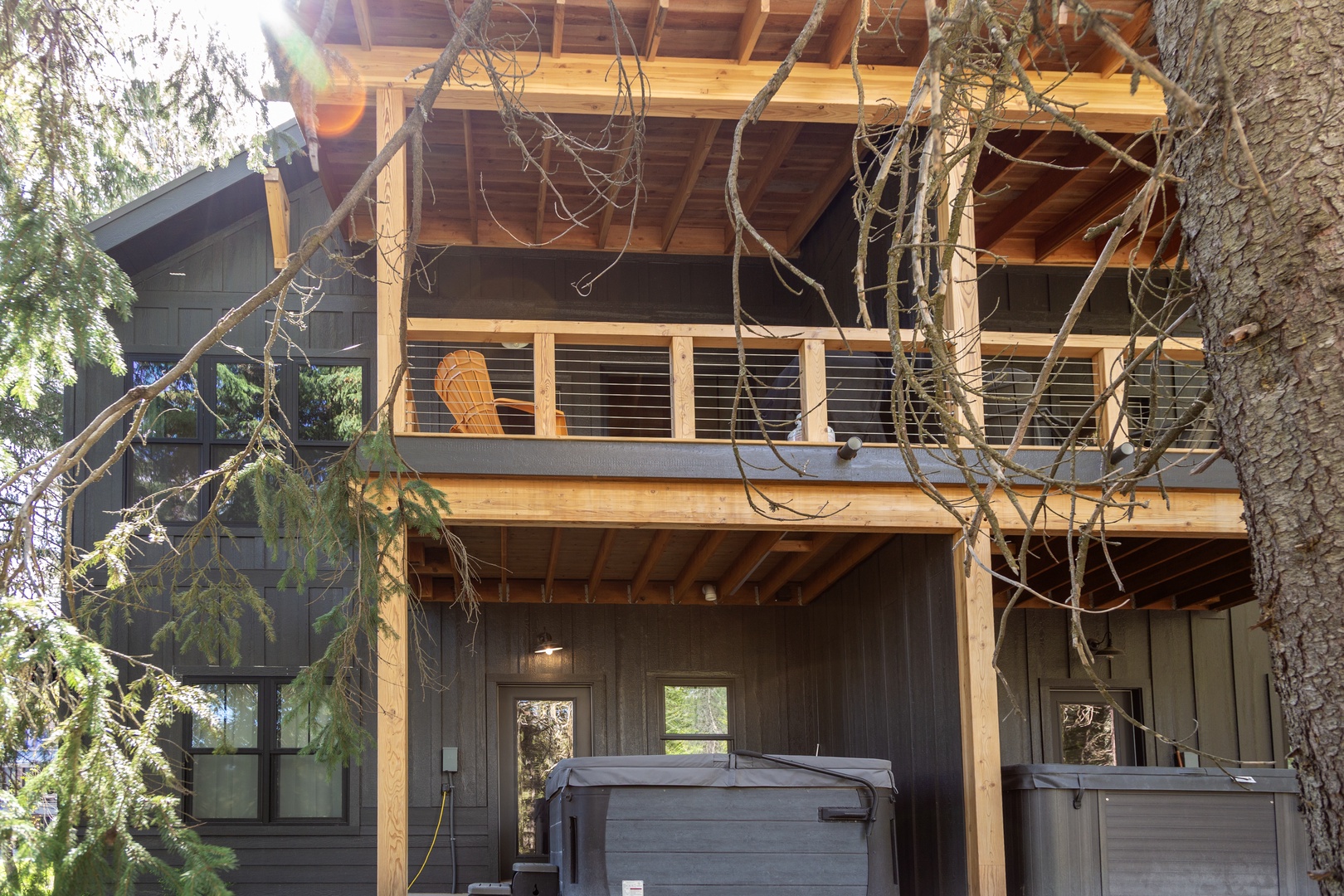 Modern mountain retreat featuring dual-level balconies and rooftop deck nestled among towering pines, with private hot tub awaiting your arrival.