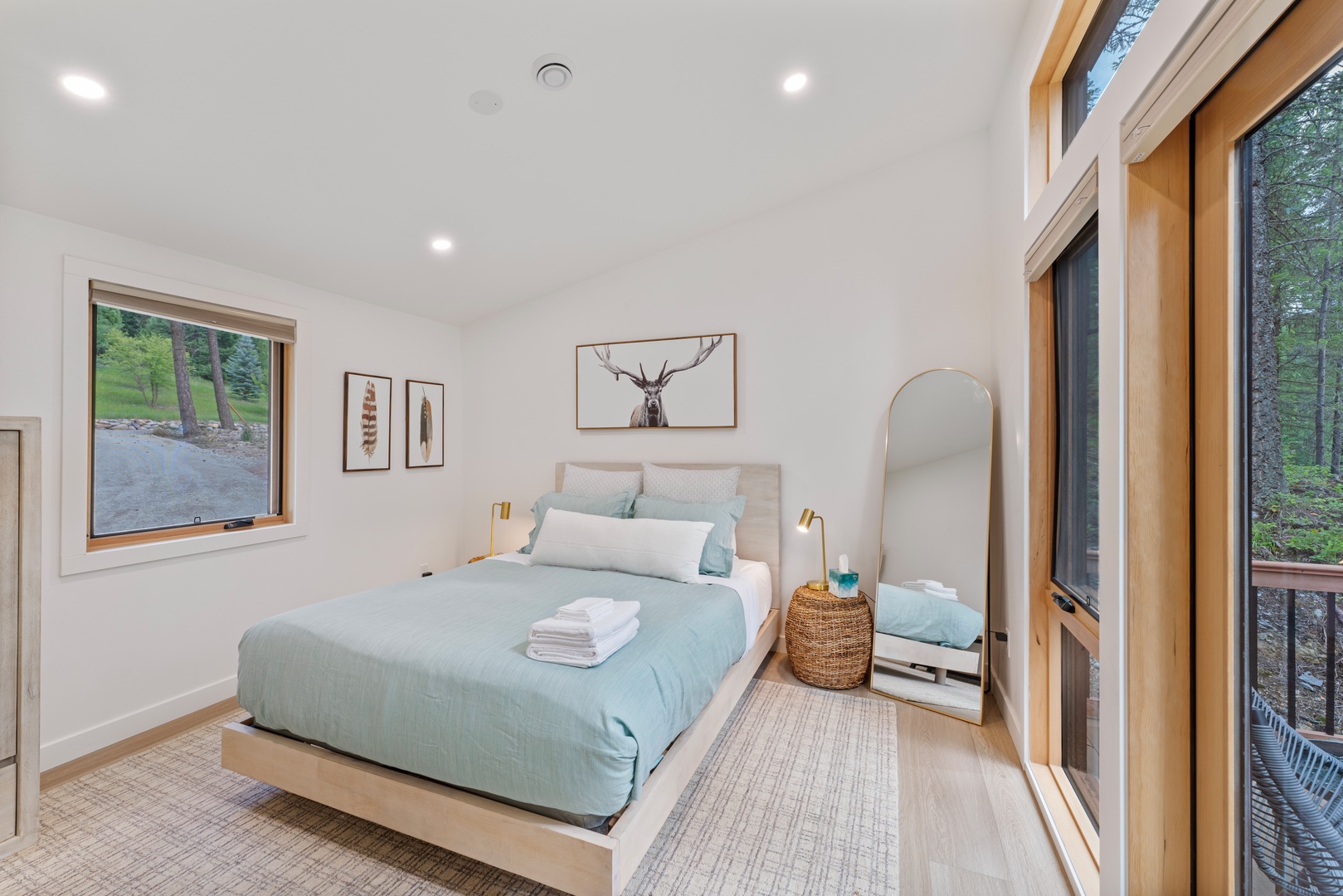 Relax in your serene bedroom with soft aqua linens, warm wood accents, and floor-to-ceiling windows framing peaceful forest views. Fresh towels await your arrival.