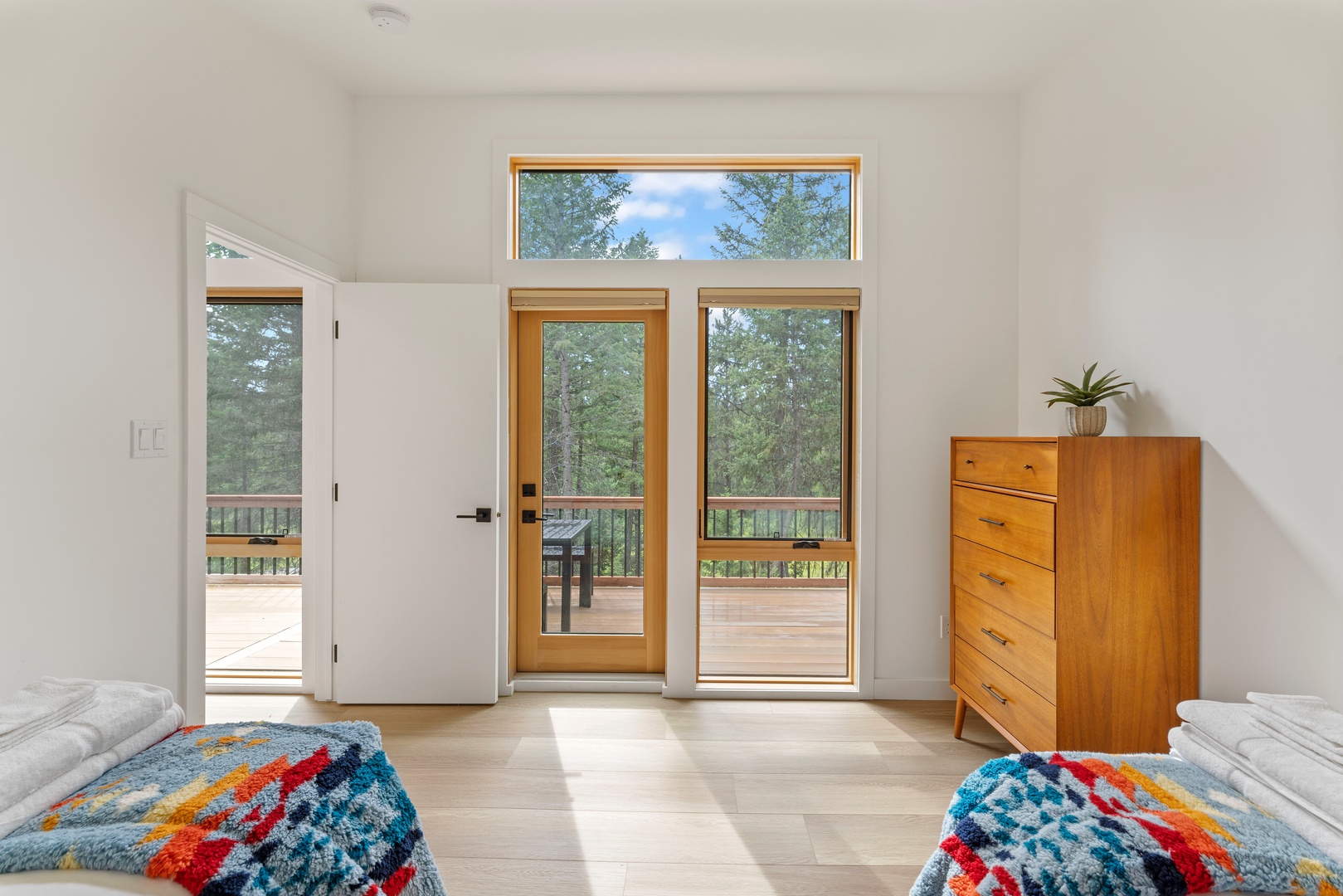 Step into your tranquil bedroom retreat where natural light pours through floor-to-ceiling glass doors, framing peaceful forest views. Your private balcony awaits, offering a serene escape surrounded by towering trees.