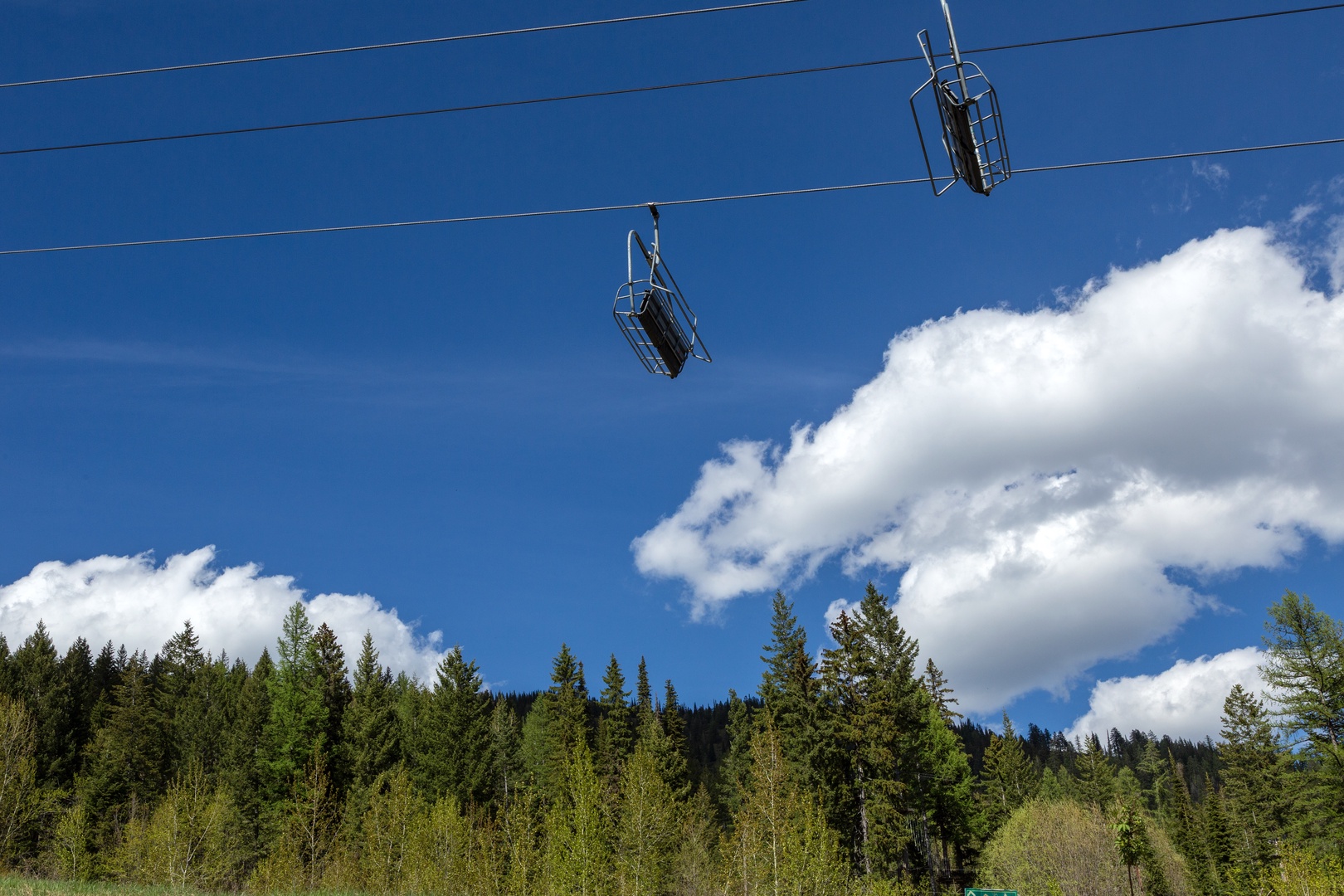 Scenic mountain chairlift ascending over lush evergreen forest under a brilliant blue sky—offering access to alpine adventures during your stay.