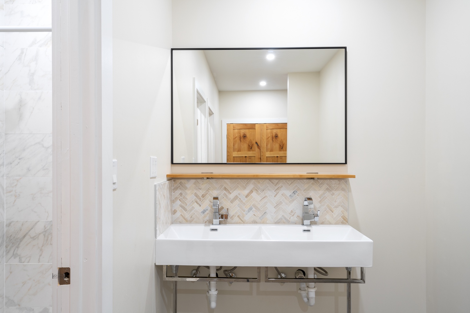 Sleek double vanity with herringbone tile backsplash and modern fixtures offers you a spa-like morning routine. Natural wood shelf and storage cabinets reflected above keep your essentials close at hand.