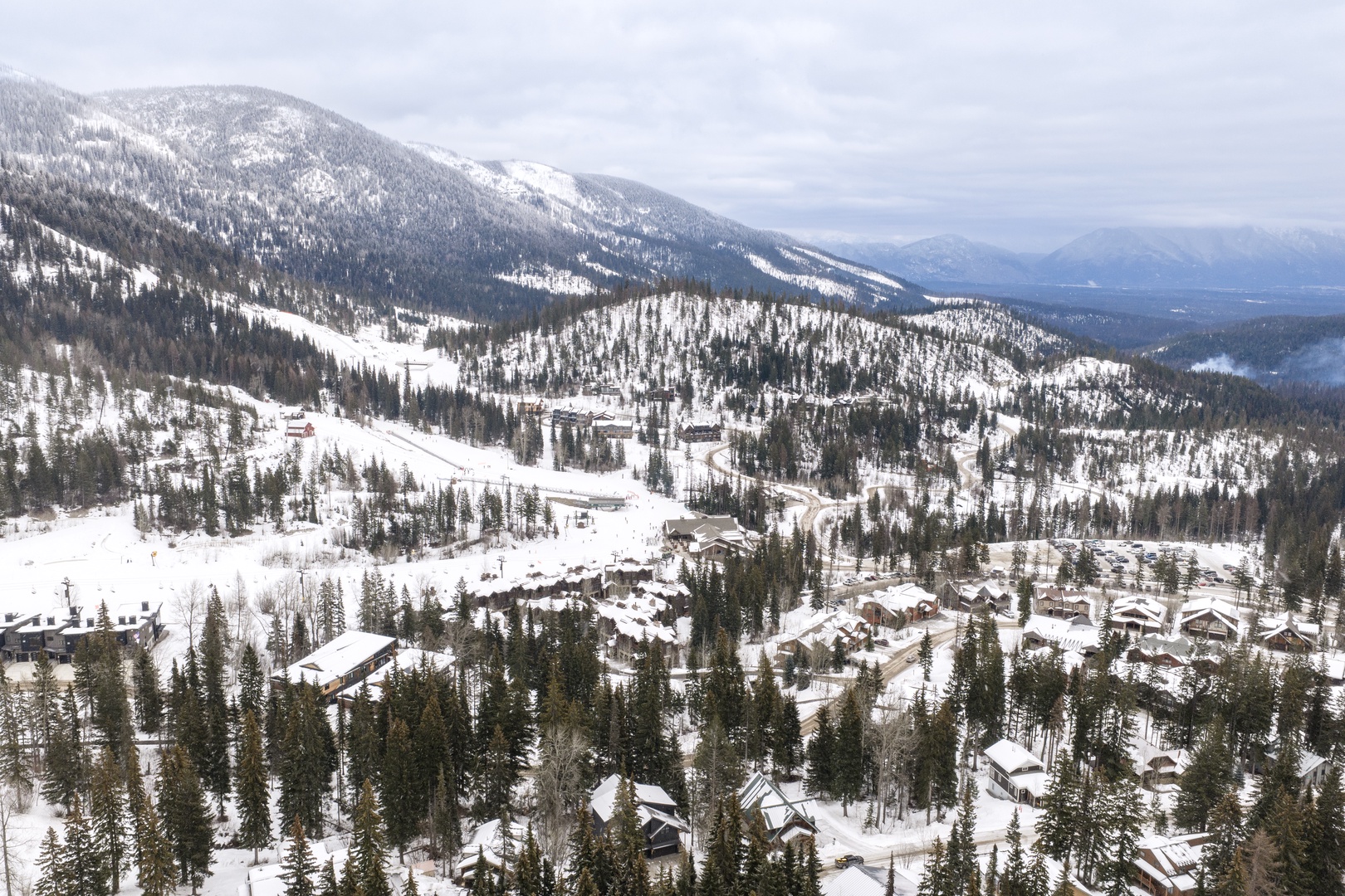 Stunning aerial view of a snow-covered mountain resort village nestled among pristine alpine forests and ski slopes.