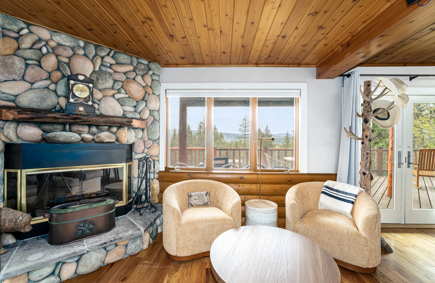 Cozy living room with rustic stone fireplace, vaulted wood ceilings, and plush seating overlooking mountain views through large windows and balcony access.