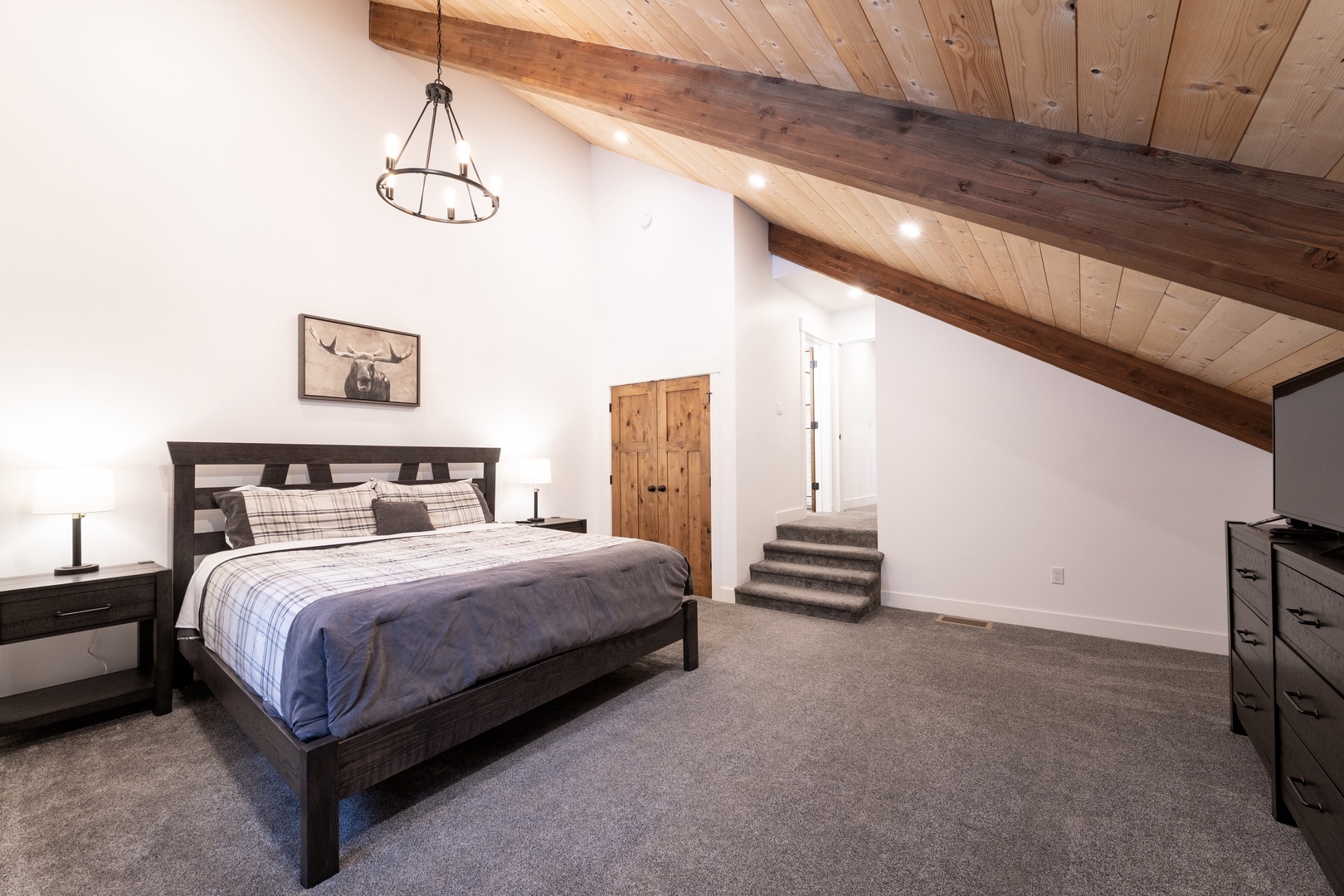 Drift off under rustic wood beams in your cozy loft bedroom, where plaid bedding and warm lighting create the perfect mountain retreat atmosphere.