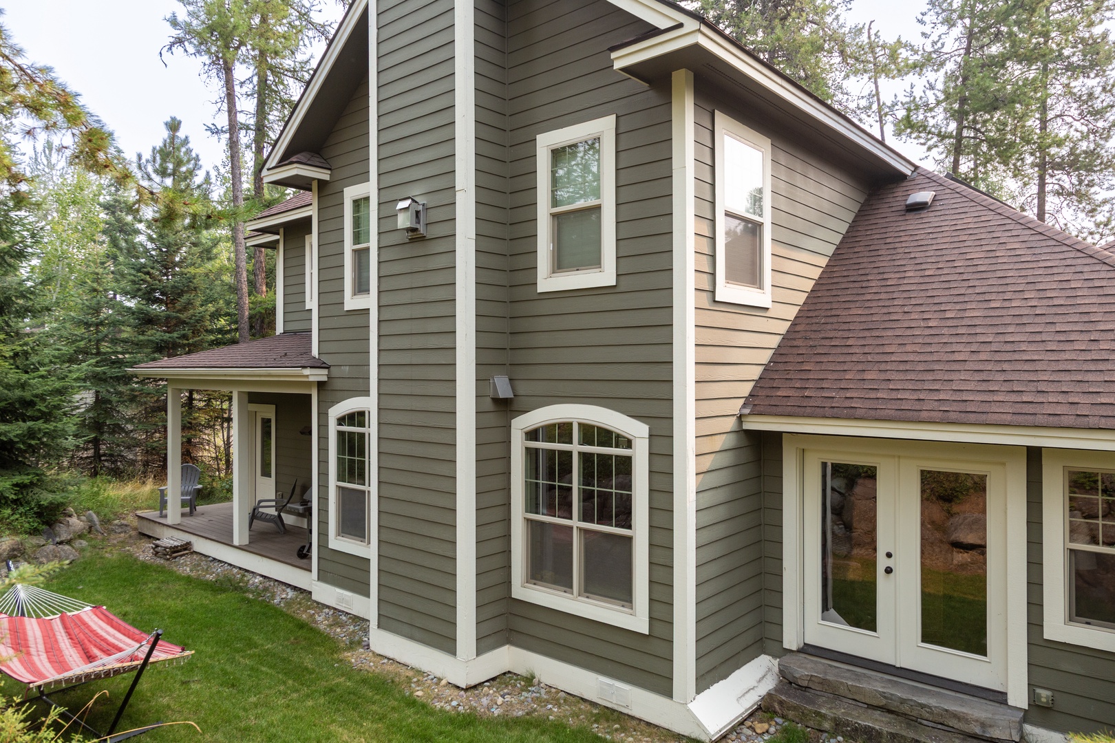 A well-appointed two-story vacation retreat nestled among towering pines, offering a peaceful woodland setting with covered porch and spacious outdoor lawn for relaxation.