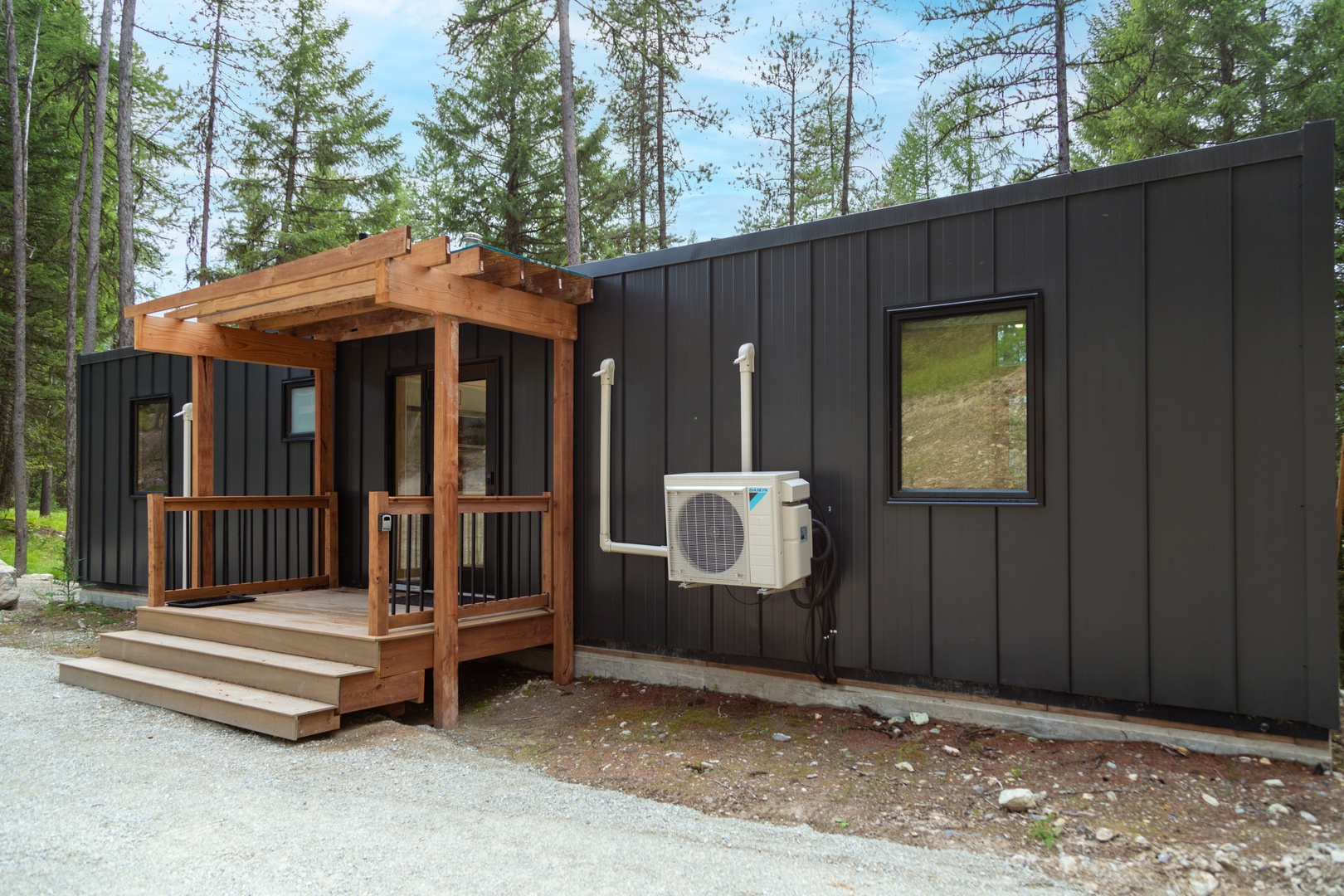 Modern cabin nestled among towering pines, featuring a welcoming covered deck and climate-controlled comfort for your forest retreat.