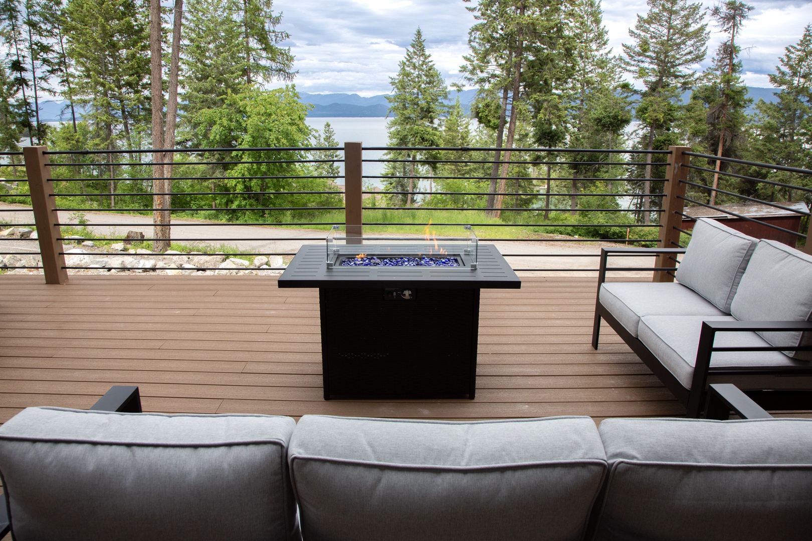 Stunning lakeside panorama framed by towering pines, with a fire table and plush seating creating the perfect outdoor gathering space.