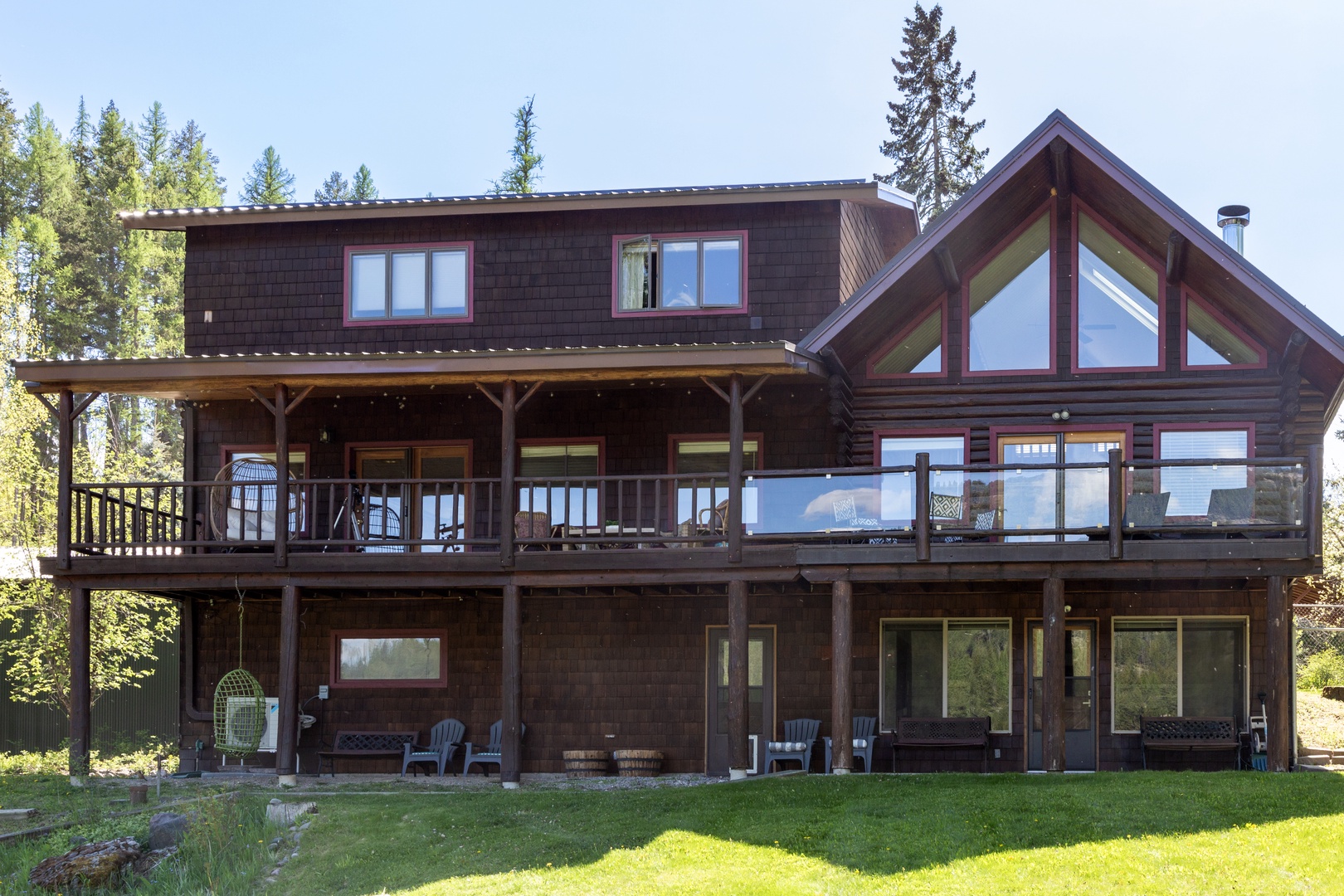 A striking mountain lodge nestled among towering pines features expansive decks and floor-to-ceiling windows framing spectacular forest views throughout this impressive multi-level retreat.