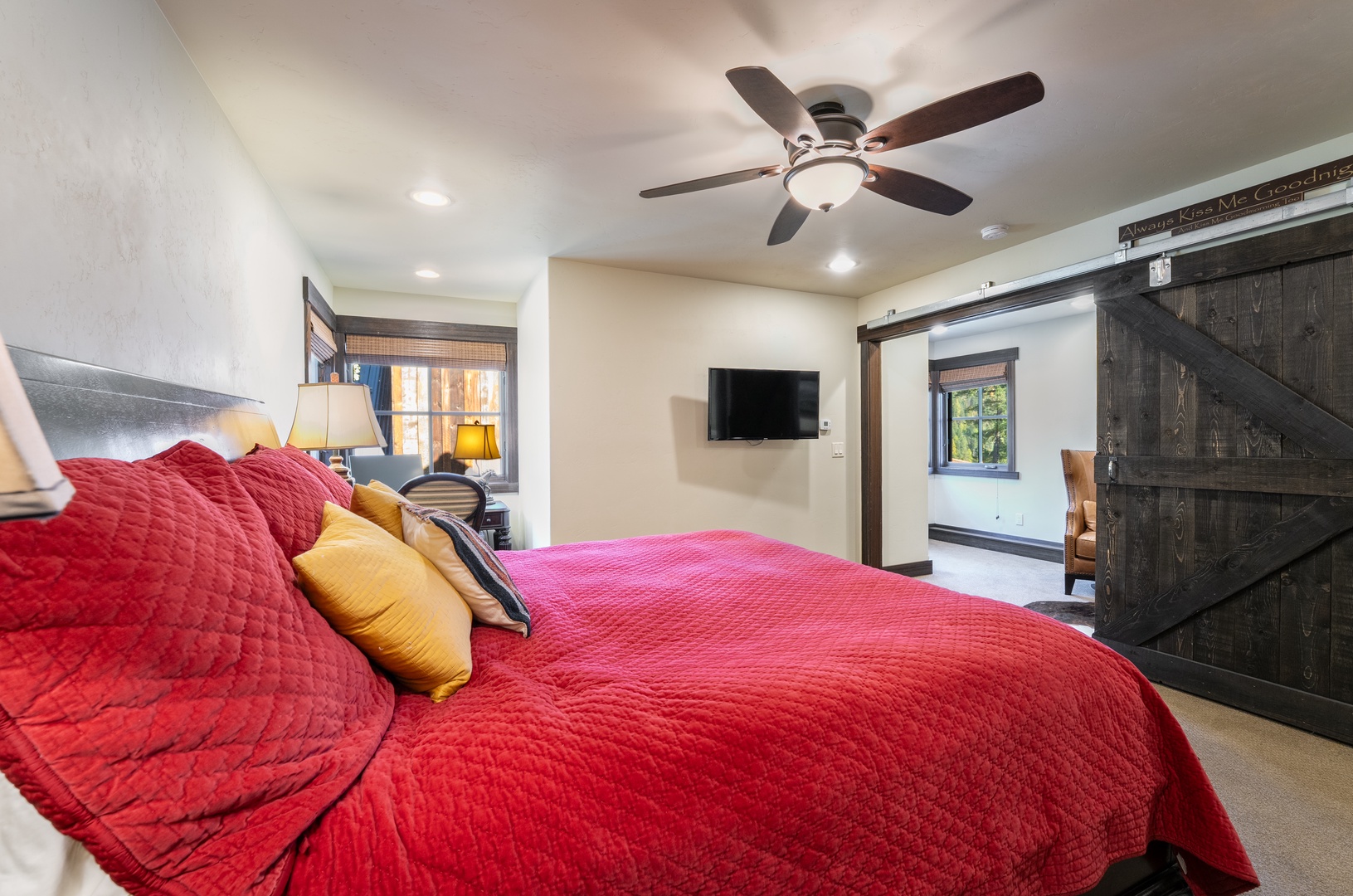Sink into this plush bed draped in rich red linens, with colorful pillows adding charm. Your room features rustic barn doors and a ceiling fan to keep you comfortable all night long.