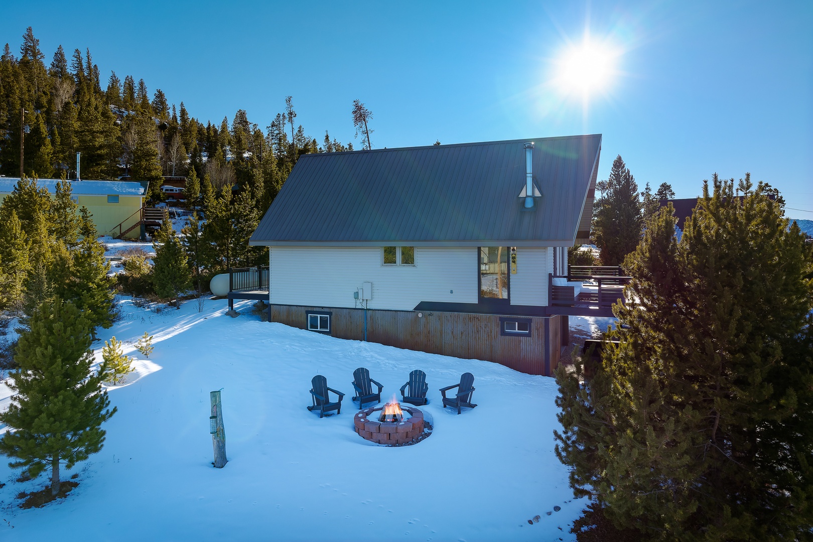 A cozy winter retreat nestled among snow-covered evergreens, featuring a fire pit surrounded by chairs for memorable mountain evenings.