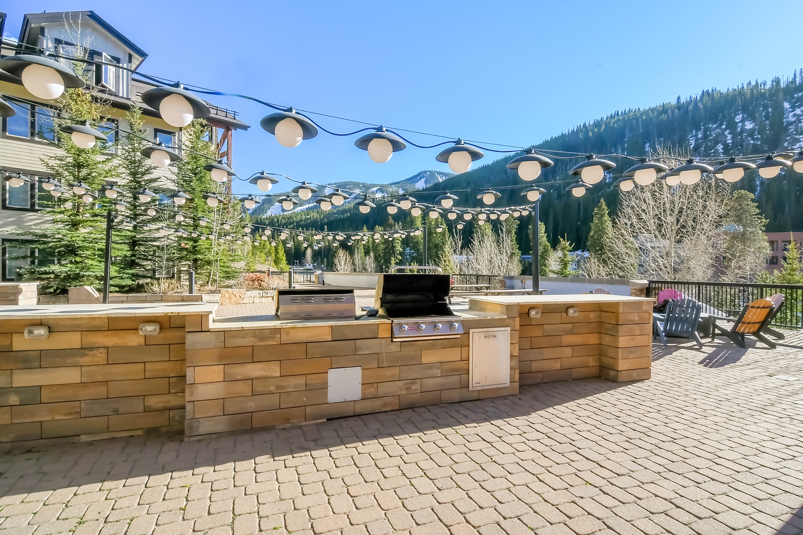Outdoor Shared BBQ station on Amenity Deck featuring stone countertops and stainless steel grill, perfect for mountain-view cooking under festive string lights.