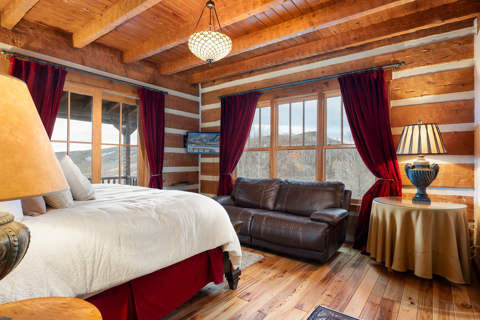 Unwind in your rustic log cabin bedroom with King bed and mountain views through expansive windows.