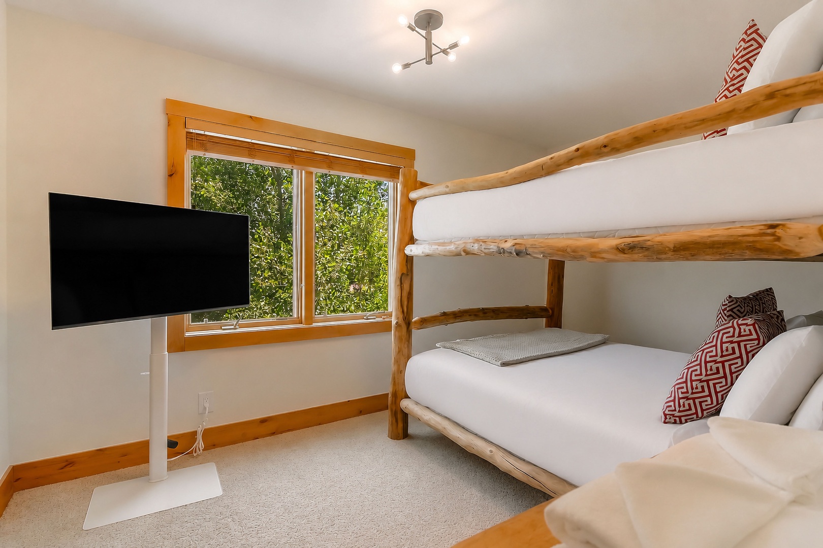 Your cozy bunk room overlooks lush greenery through warm wood-framed windows, with crisp linens and a flat-screen TV for relaxing evenings together.