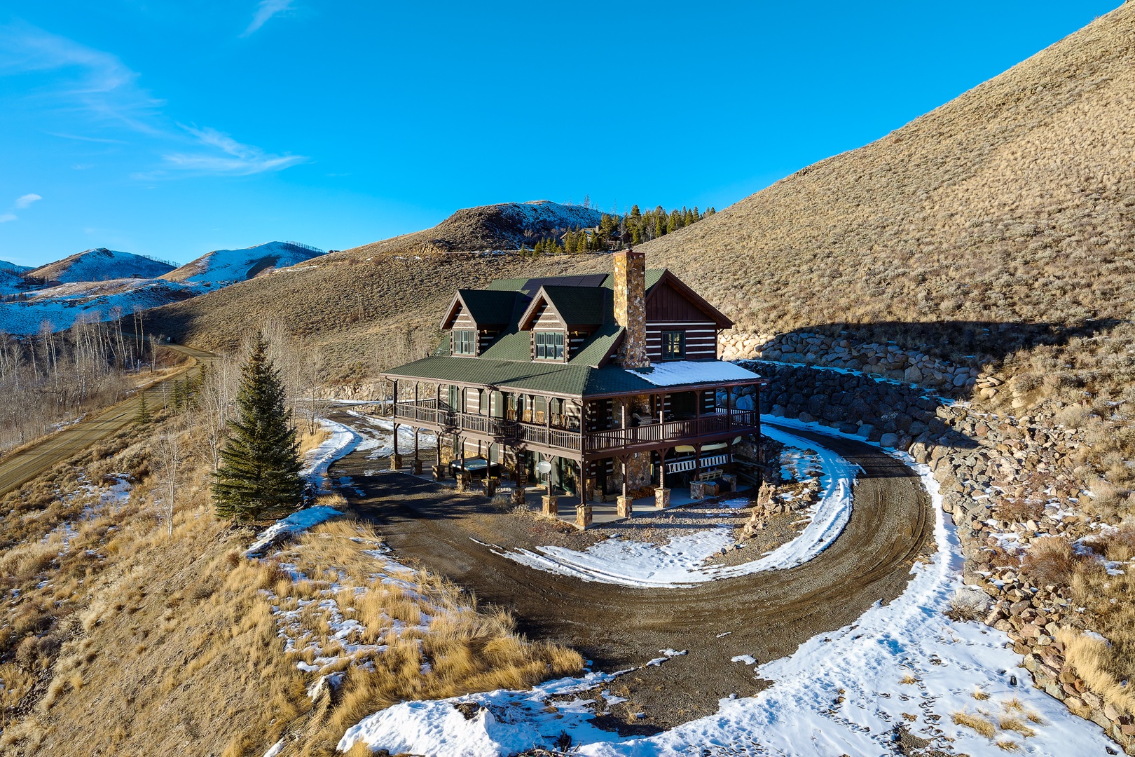 Mountain lodge nestled in pristine wilderness with winter snow patches and panoramic alpine views.
