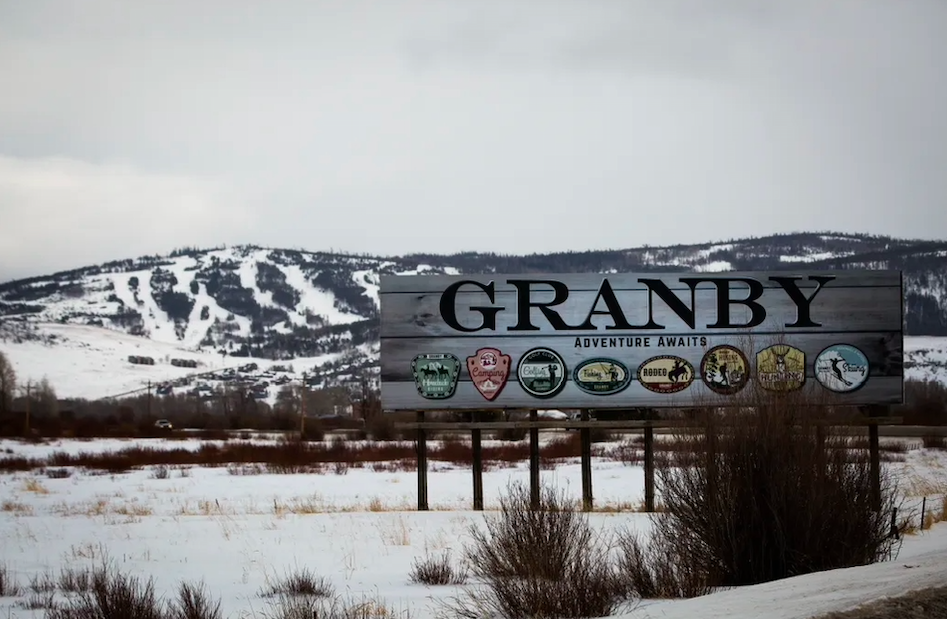 Granby welcome sign marks your arrival to this mountain town, with snow-covered ski slopes rising dramatically in the background.
